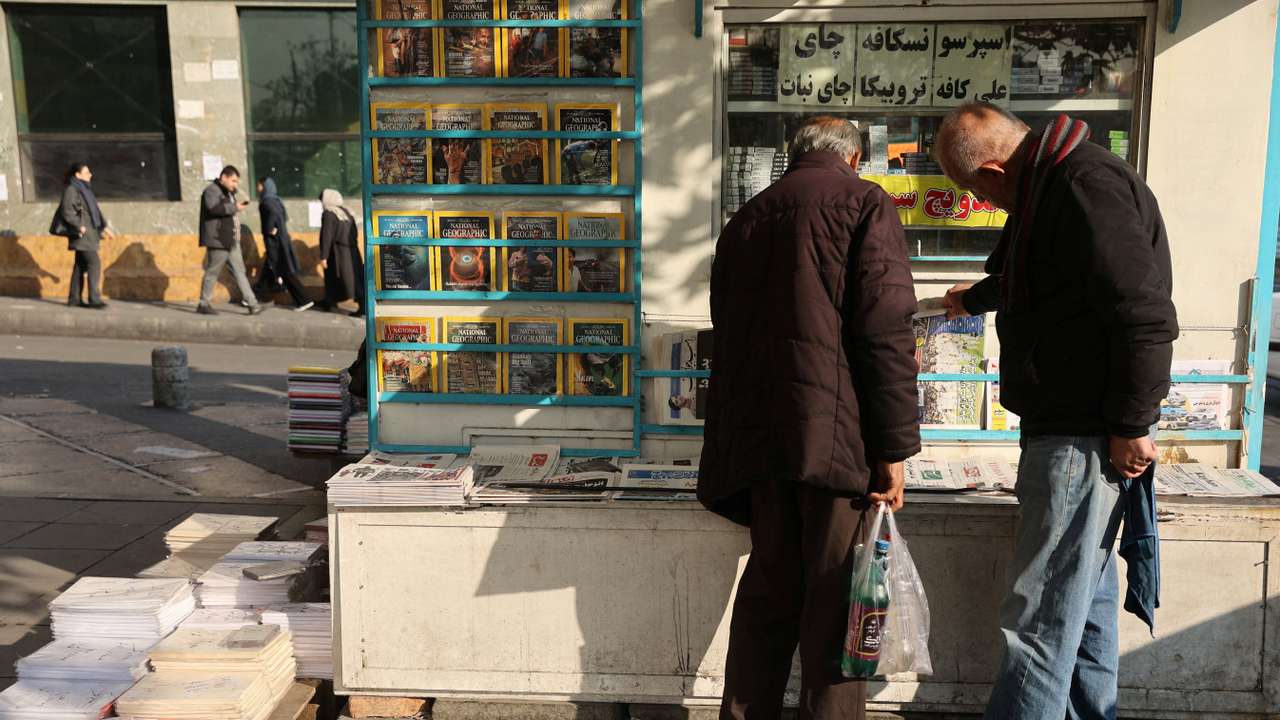 Iranian men read newspapers on a street, as protests erupt over the collapse of the currency's value, in Tehran