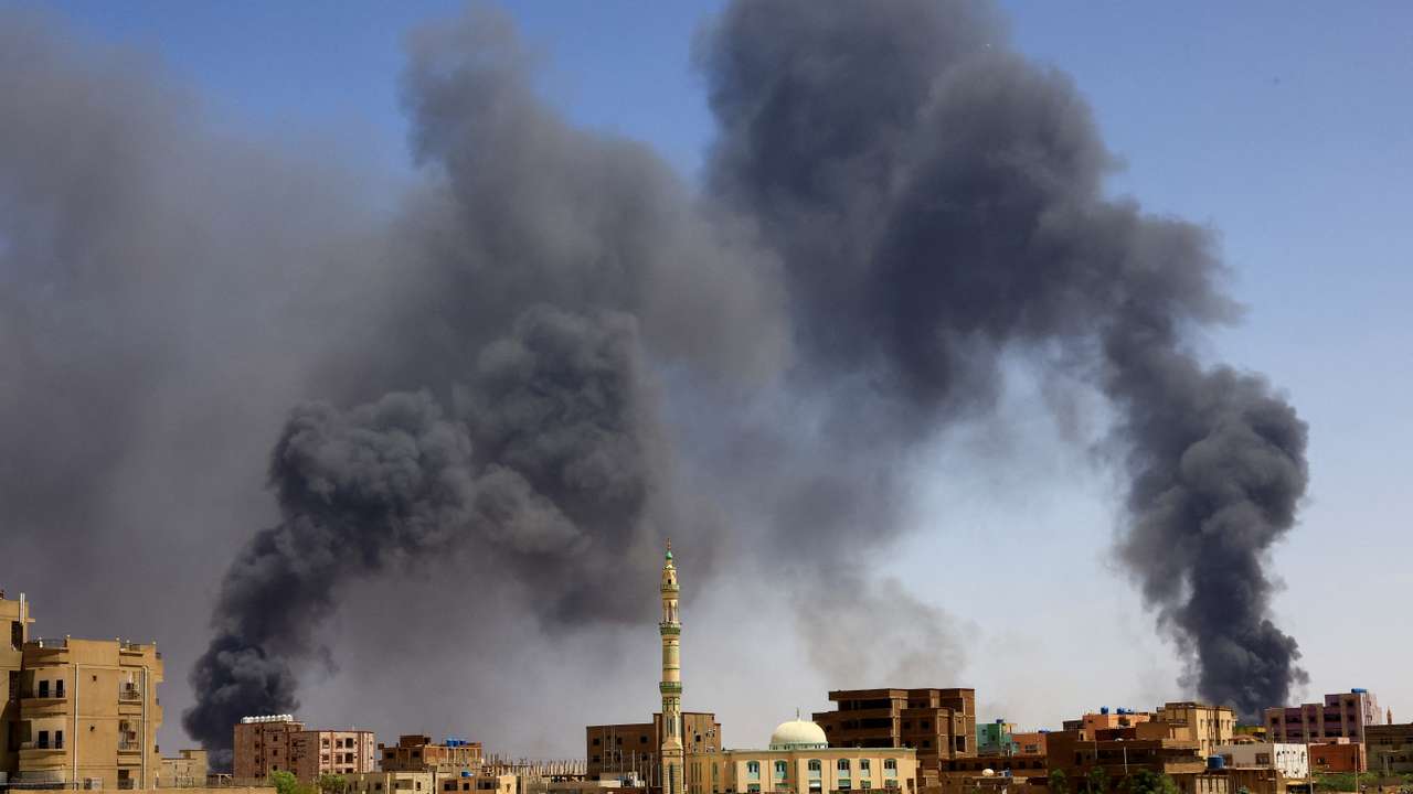 Man walks while smoke rises above buildings after aerial bombardment in Khartoum North