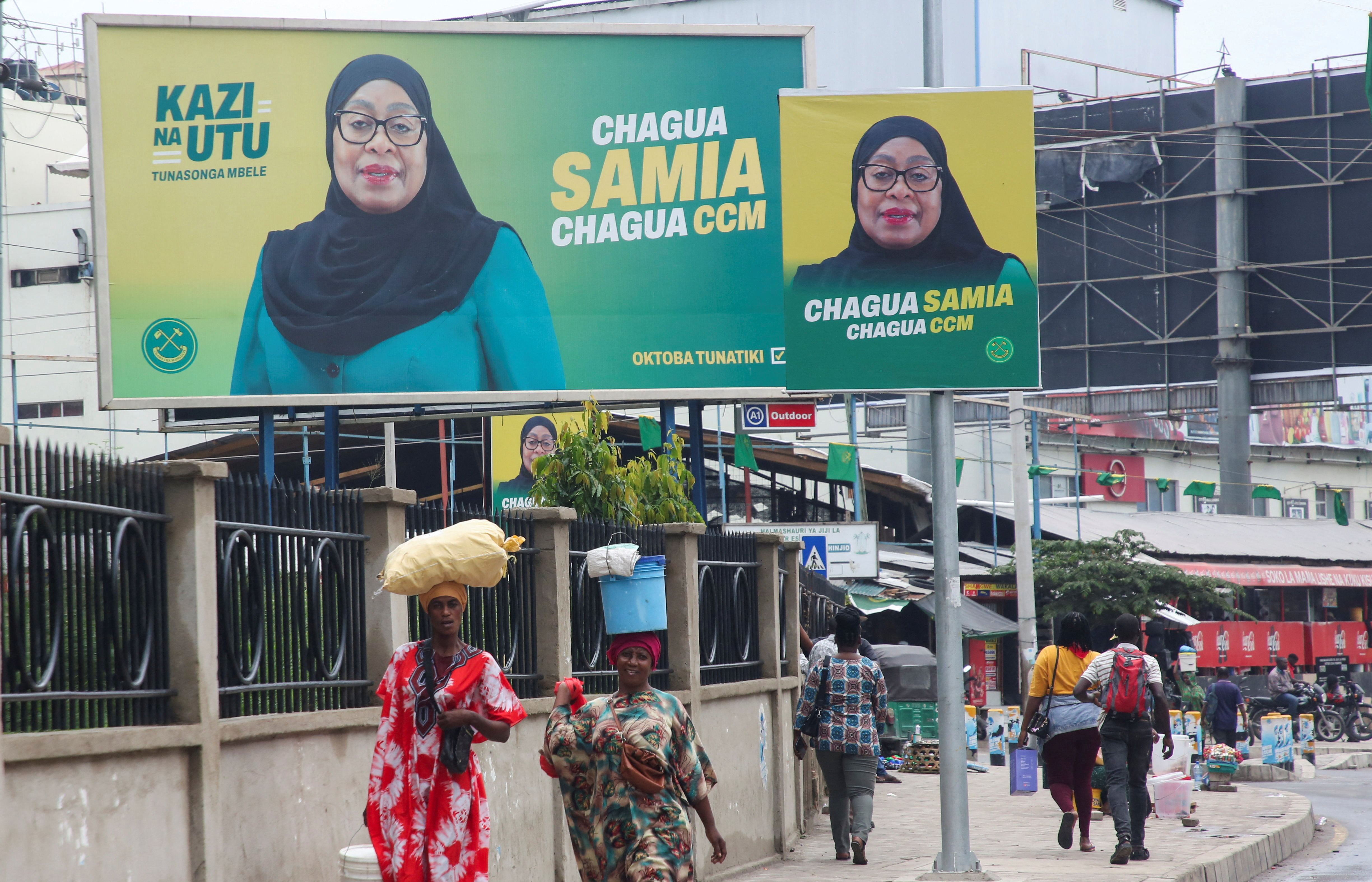 People walk past electoral campaign billboards of Tanzania's President Samia Suluhu Hassan of the ruling CCM ahead of the general elections in Ilala district of Dar es Salaam