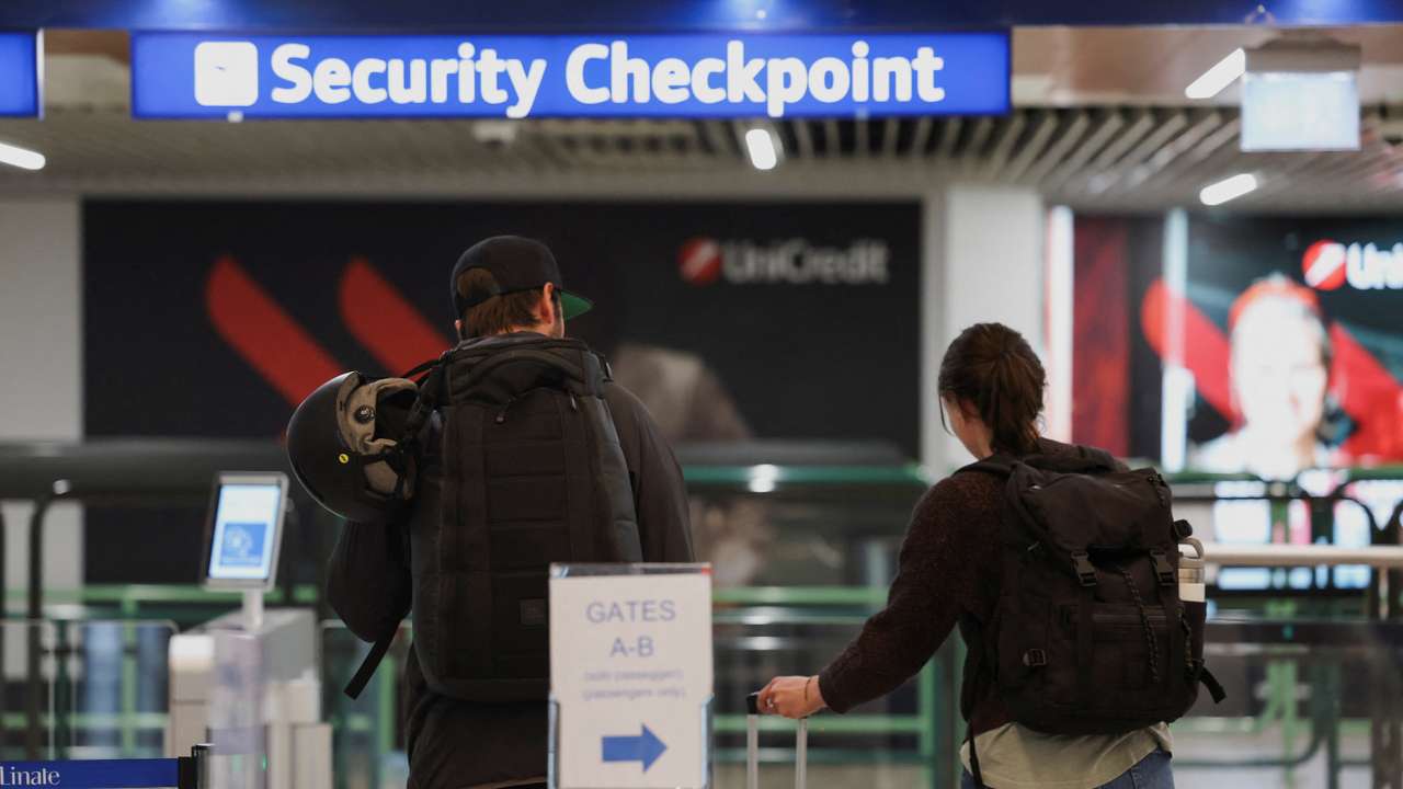 People walk next to a document verification checkpoint at Linate Airport in Milan