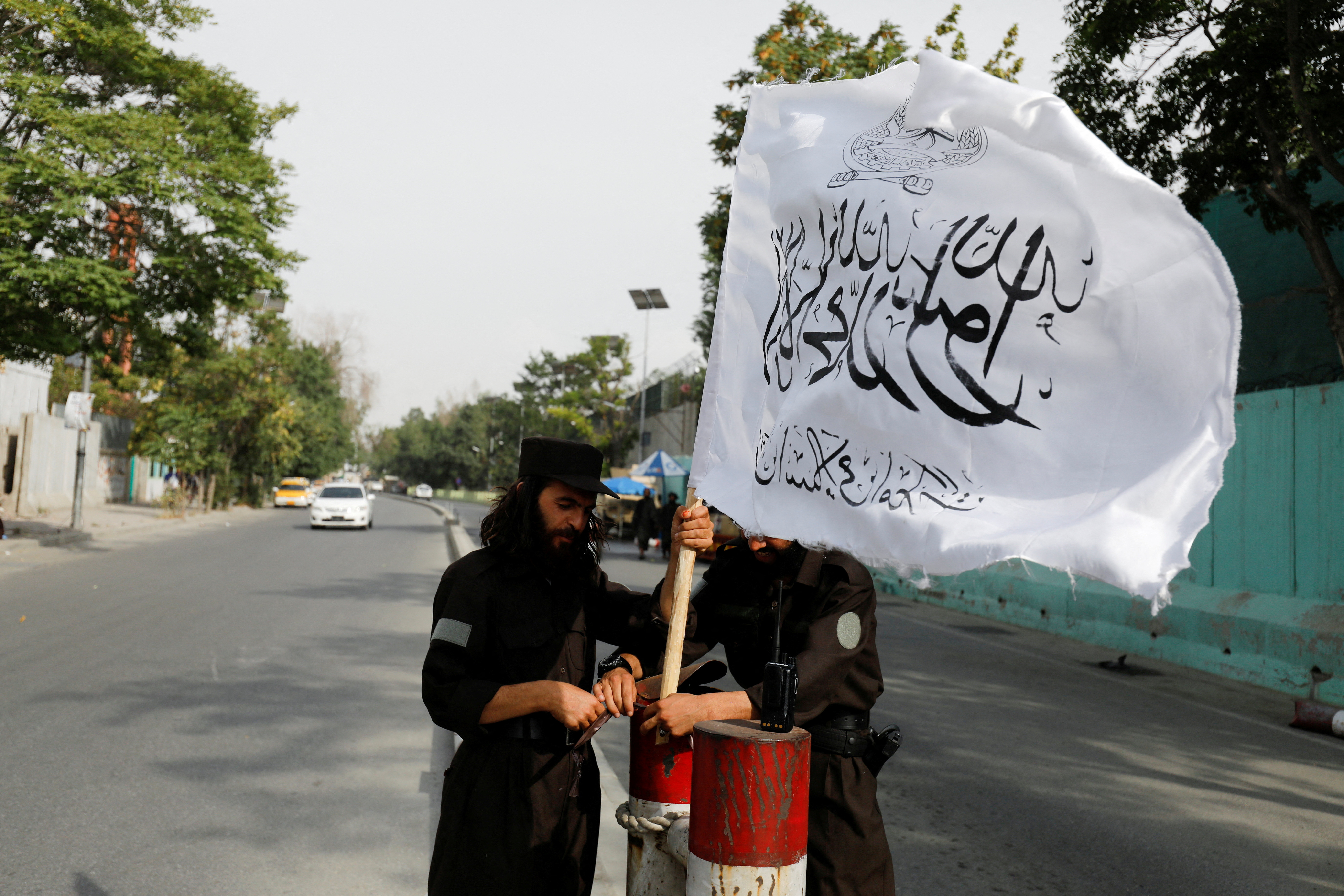 FILE PHOTO: Taliban fighters install a Taliban flag on a checkpoint in Kabul
