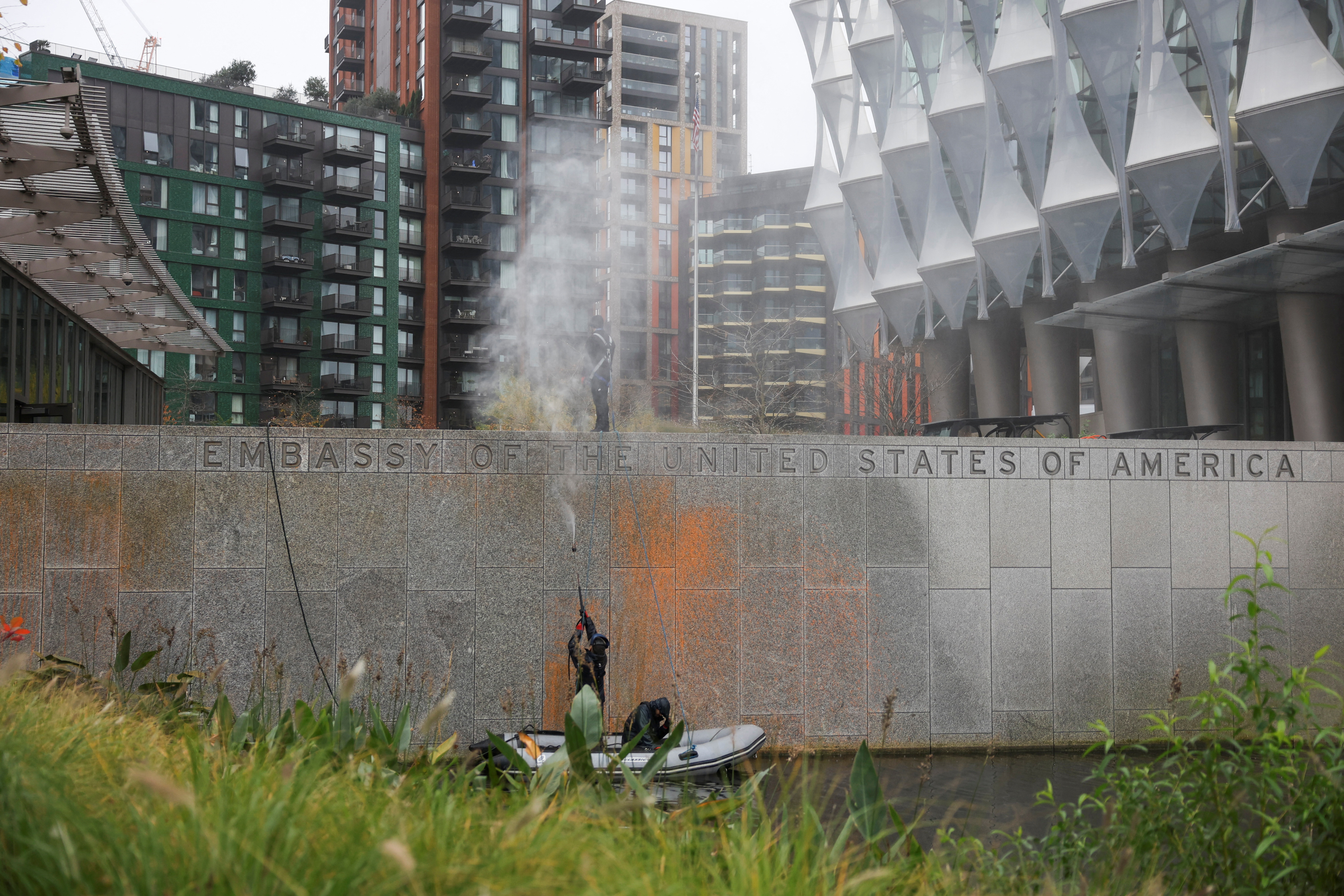 People use a pressure washer to wash orange paint off a sign outside the U.S. embassy in London