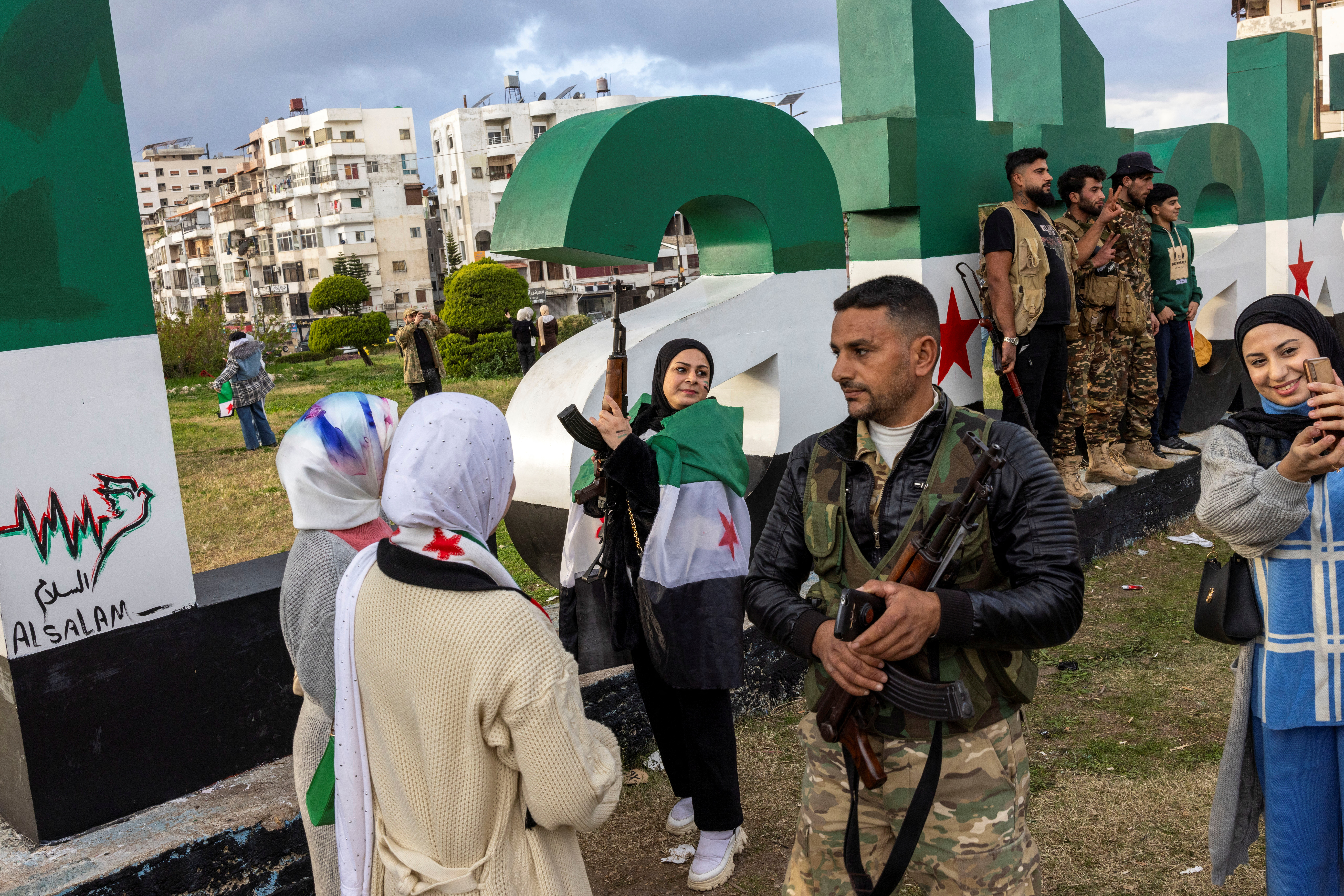 People take selfies with flags and rifles borrowed from fighters of the ruling Syrian body at a square in central Latakia