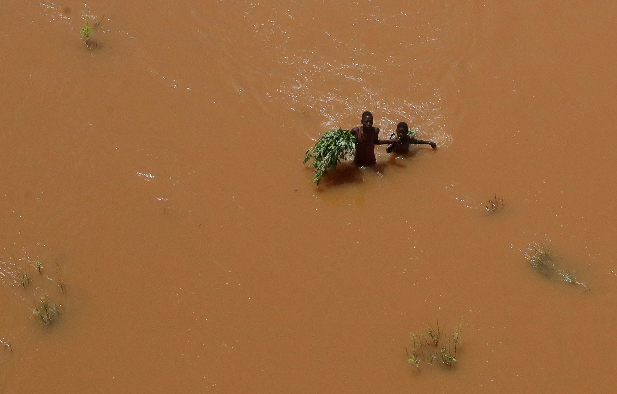 FILE PHOTO: People hold on to plants as they wade through flood waters after they were displaced following heavy rains in Garsen