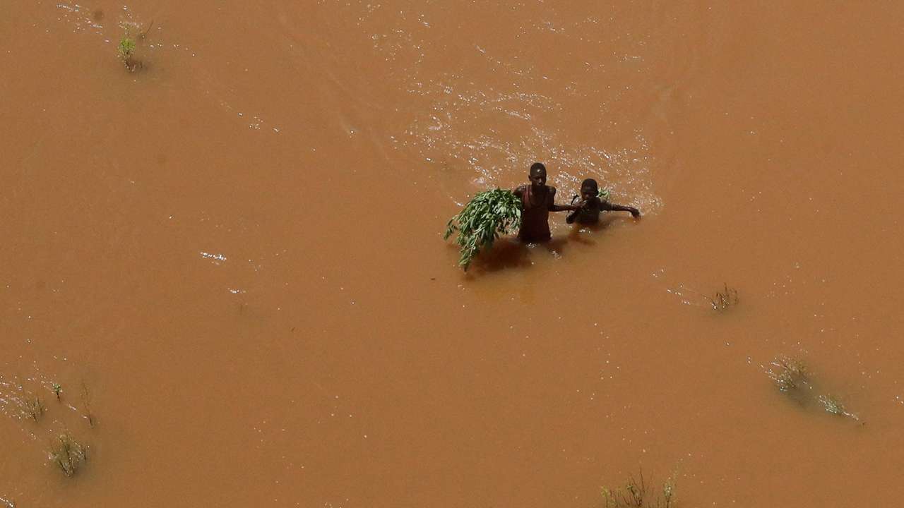 FILE PHOTO: People hold on to plants as they wade through flood waters after they were displaced following heavy rains in Garsen