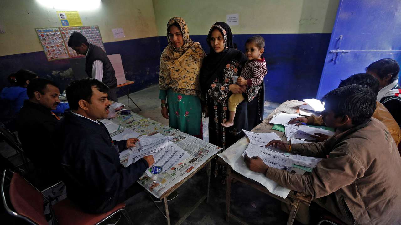FILE PHOTO: Women wait to get their voting slip from an officer at a polling booth station during the state assembly election in New Delhi