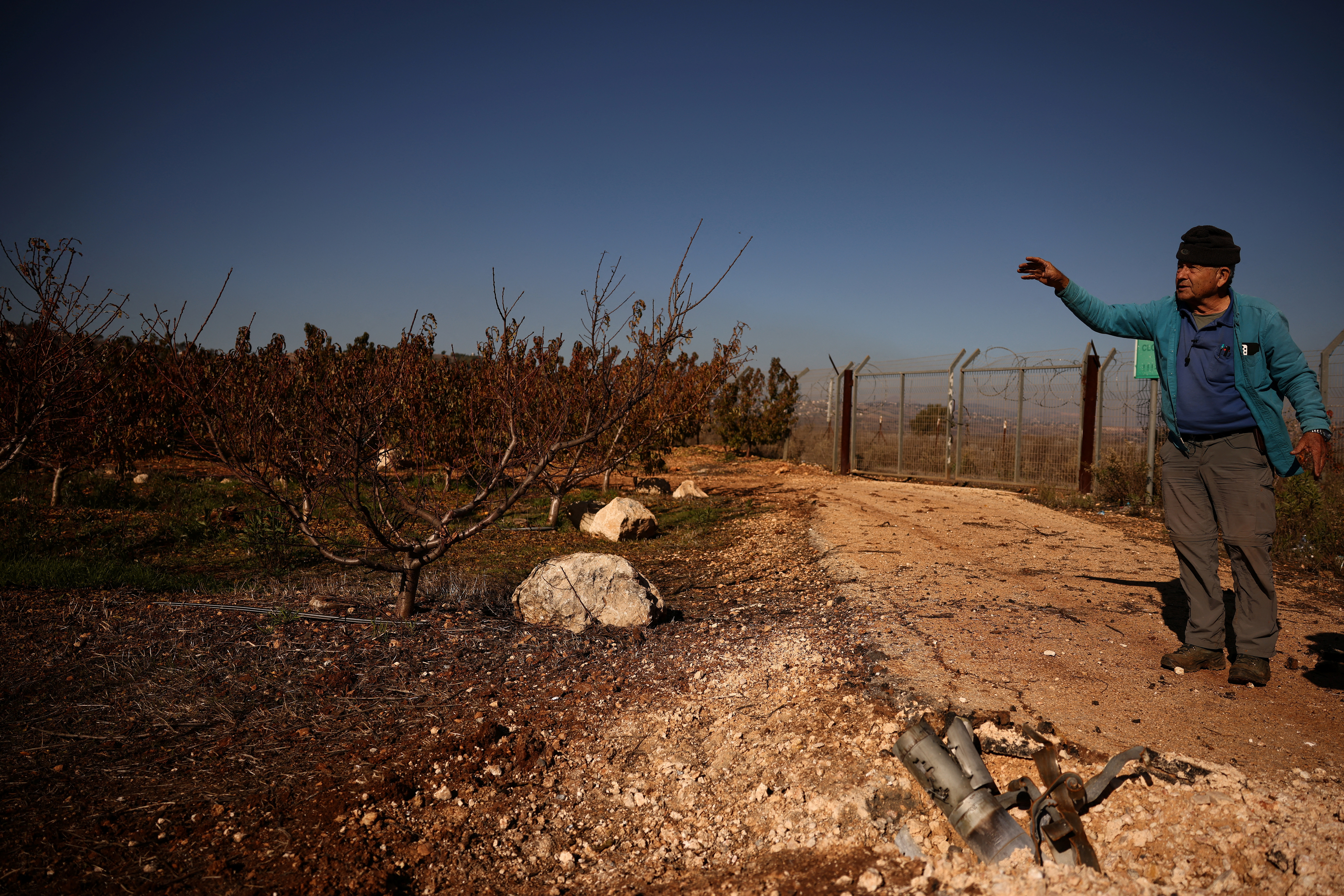 Moshe Weinstein, 76, an Israeli farmer stands near the remains of a rocket, launched from Lebanon, at his apple farm in Metula