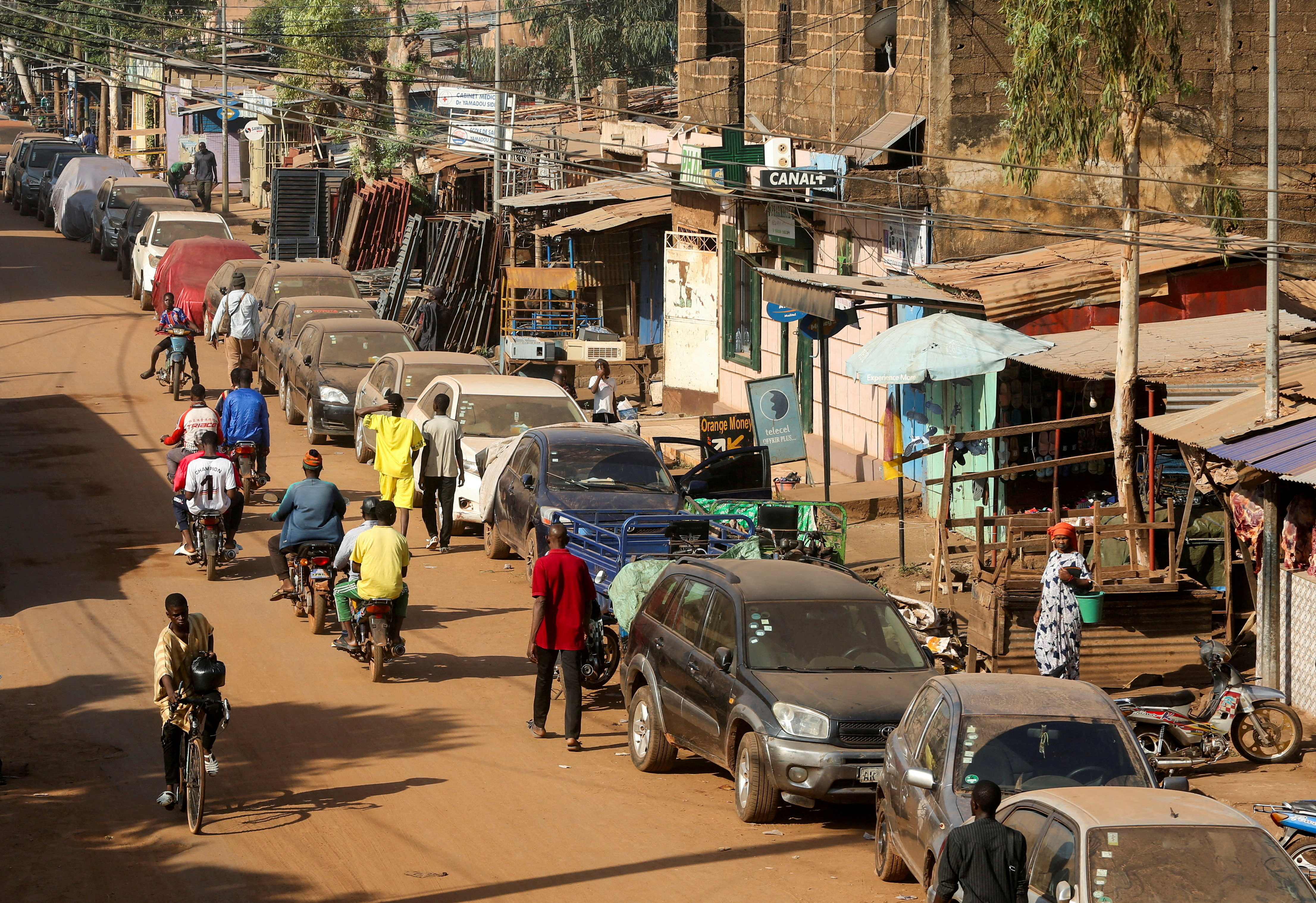 FILE PHOTO: A cyclist and motorcyclists pass by cars parked on the roadside in Bamako, Mali