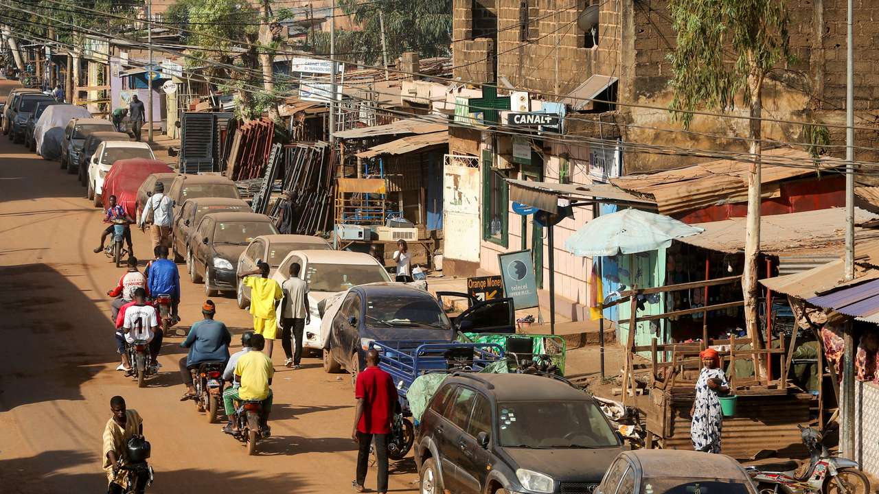 FILE PHOTO: A cyclist and motorcyclists pass by cars parked on the roadside in Bamako, Mali