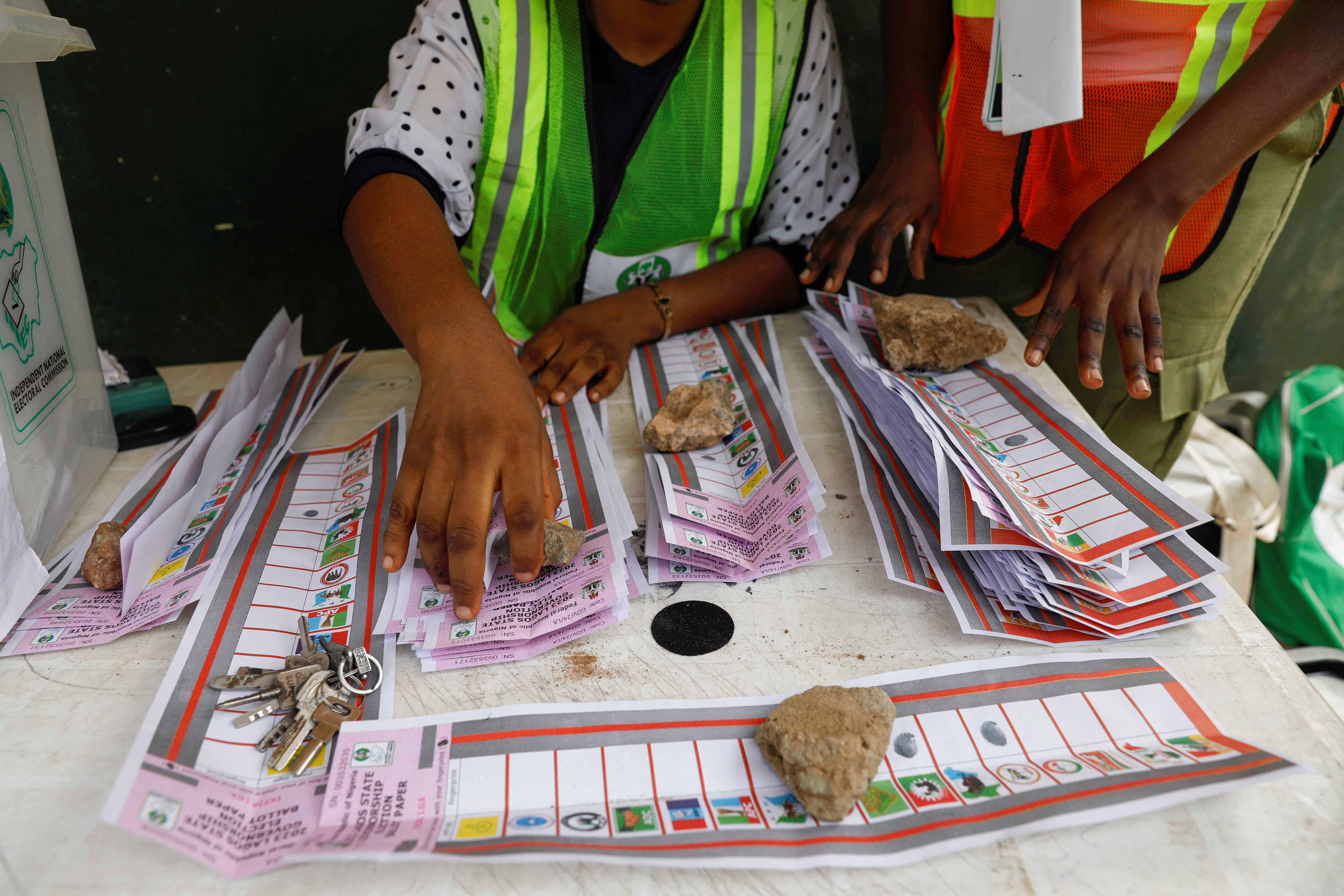 Electoral officials use stones to hold down ballots during the vote counting process of the gubernatorial election, in Lagos