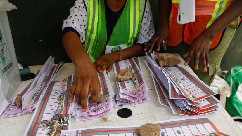 Electoral officials use stones to hold down ballots during the vote counting process of the gubernatorial election, in Lagos