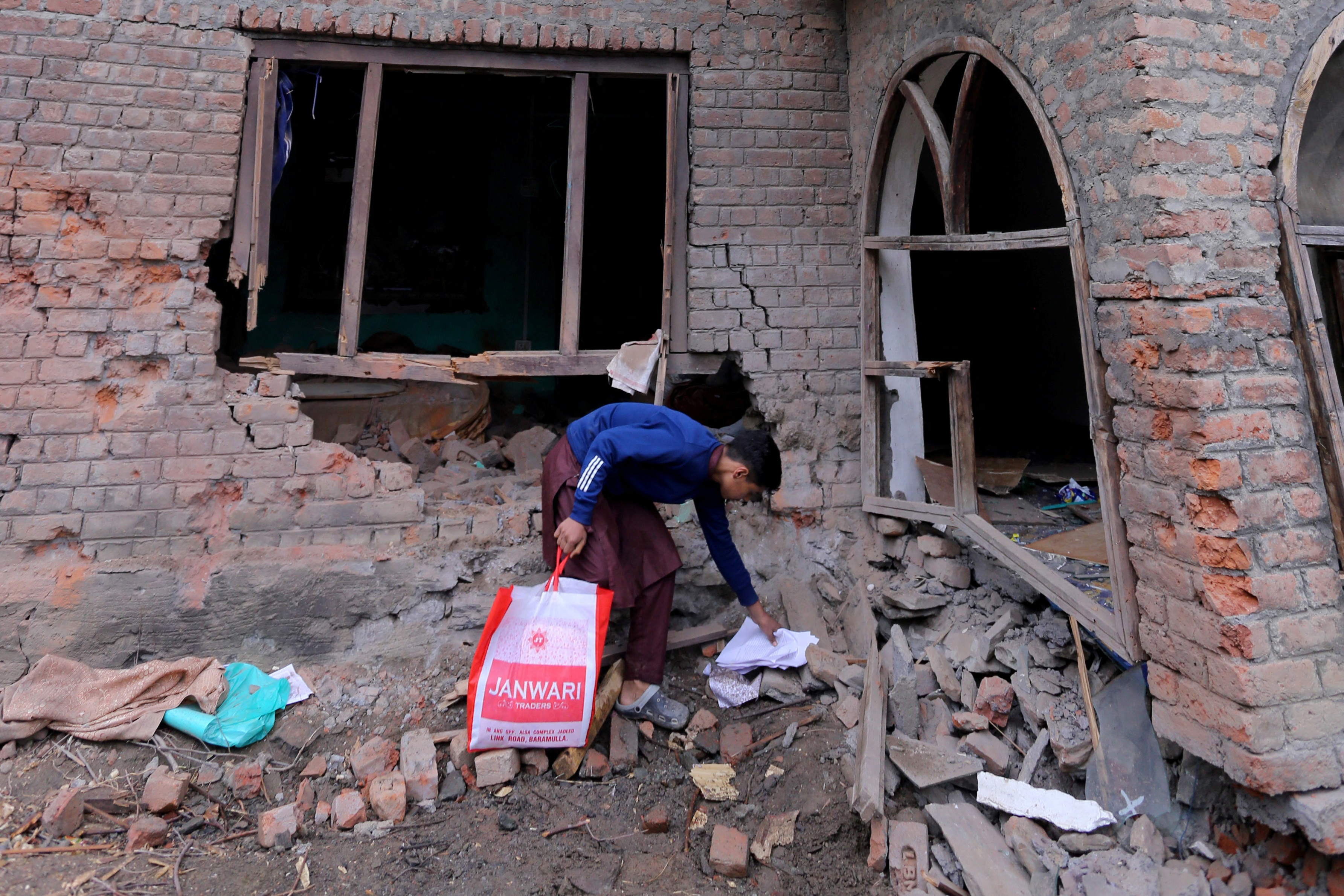 A boy collects papers from the debris of a residential house damaged by a cross-border shelling in Gingal village