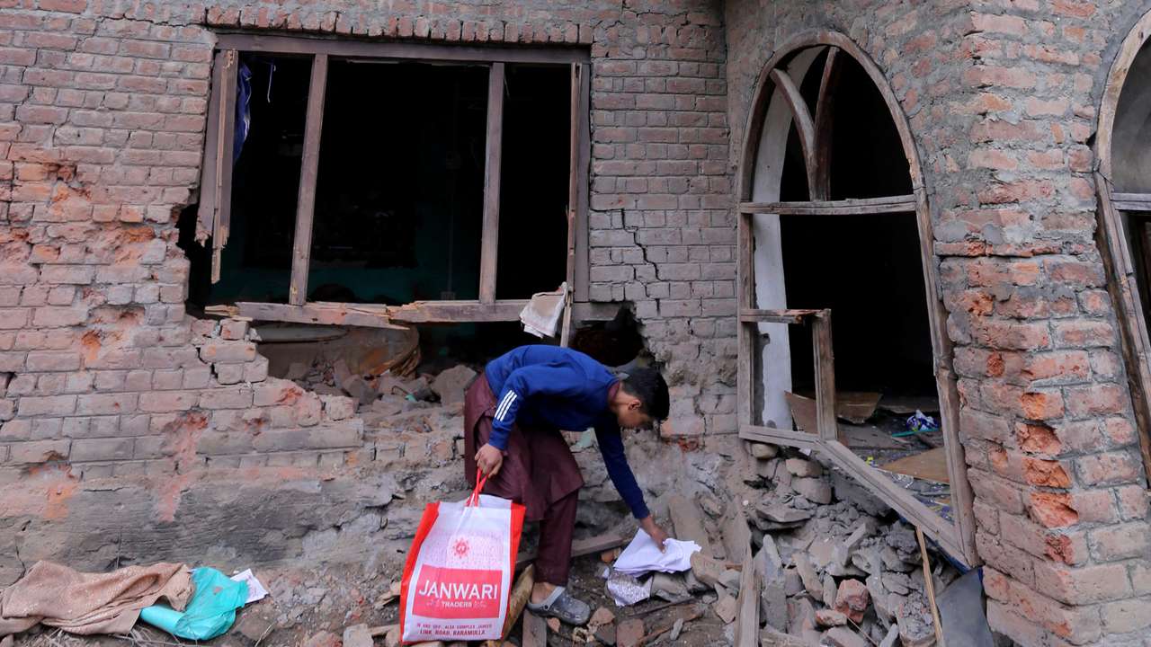 A boy collects papers from the debris of a residential house damaged by a cross-border shelling in Gingal village