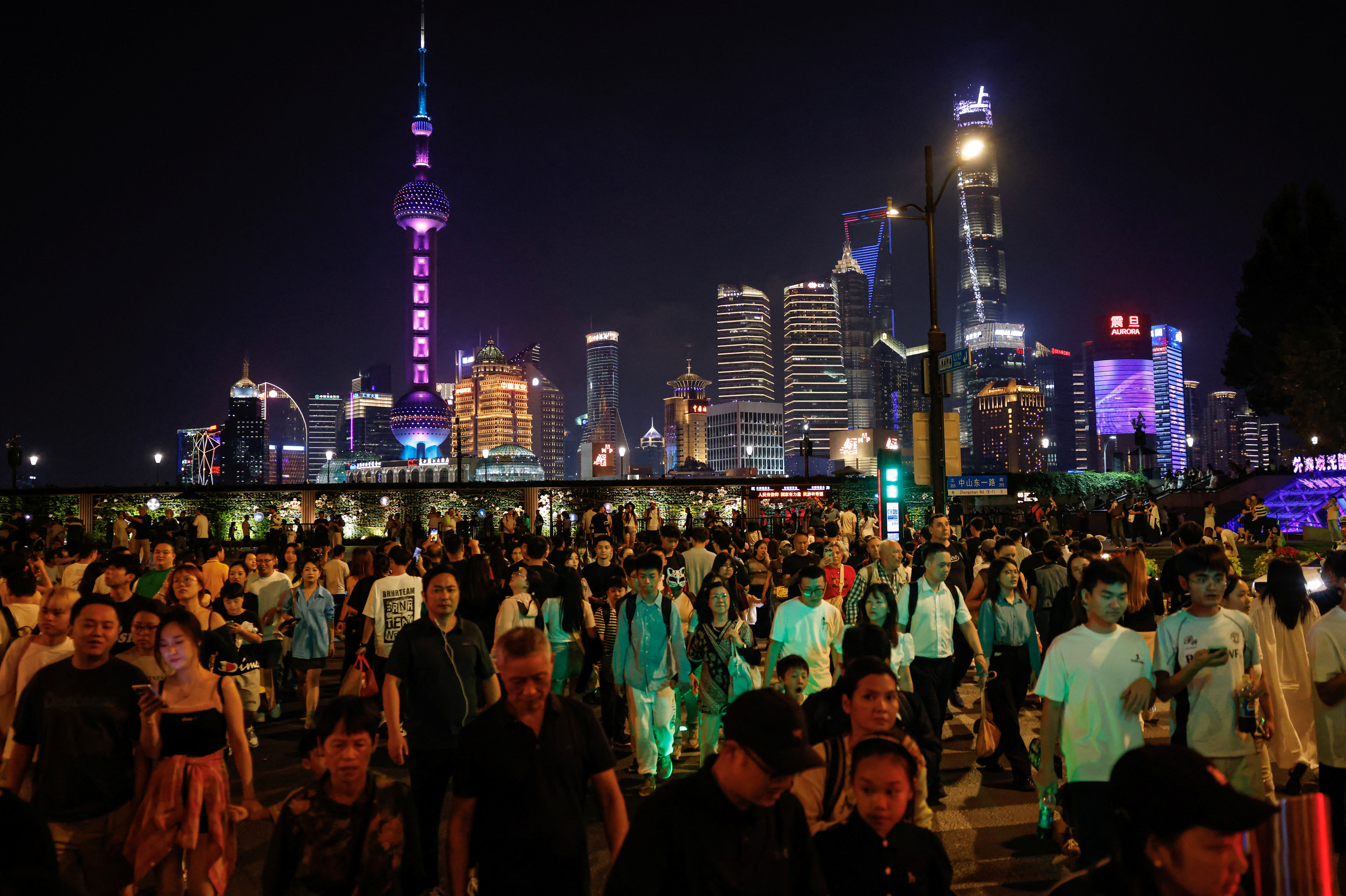 People walk across a street near the Bund with the backdrop of the financial district of Pudong in Shanghai