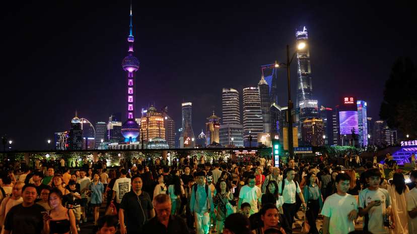 People walk across a street near the Bund with the backdrop of the financial district of Pudong in Shanghai