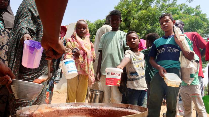 FILE PHOTO: People hold pots as volunteers distribute food in Omdurman