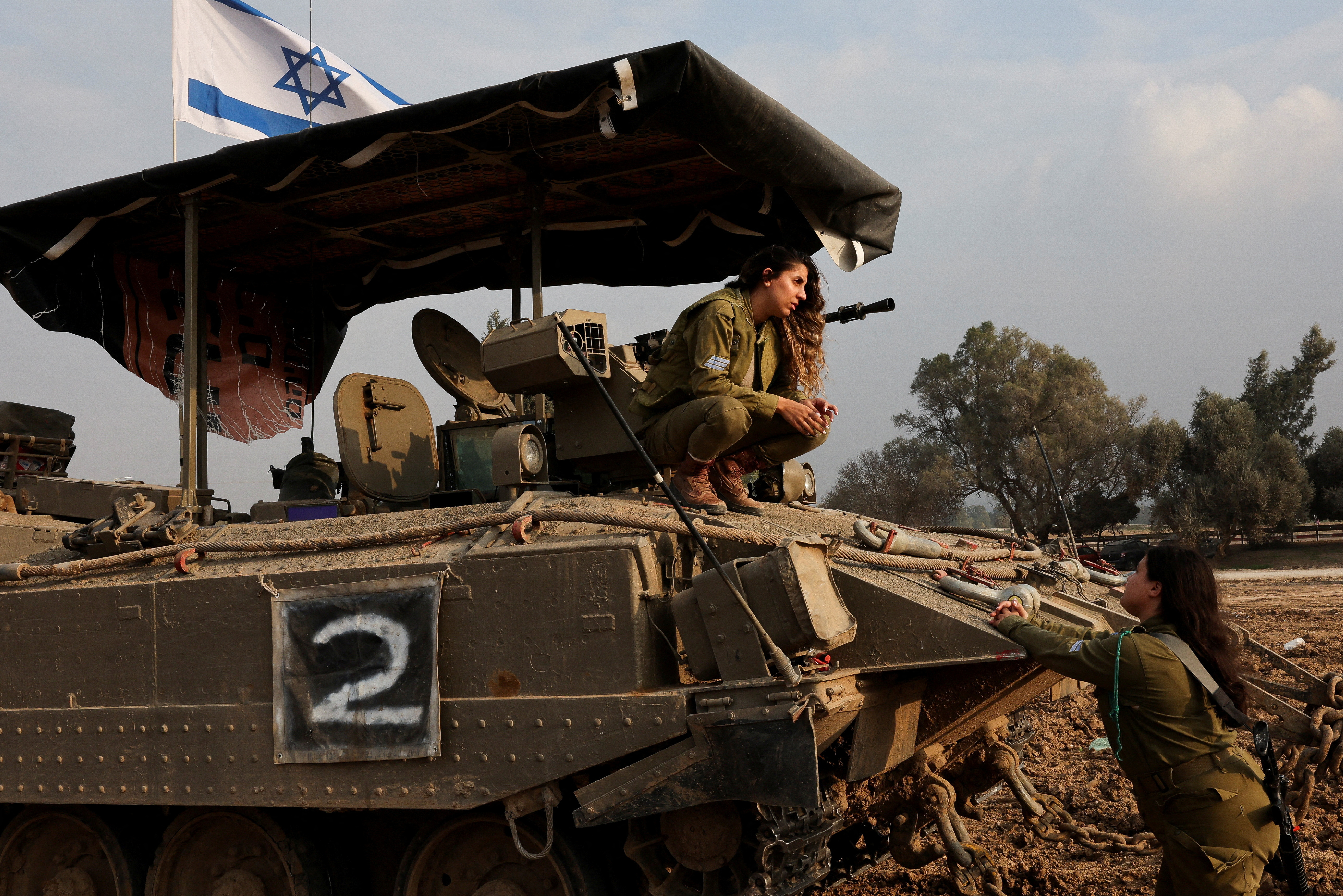An Israeli soldier crouches on an armoured personnel carrier near the Israel-Gaza border