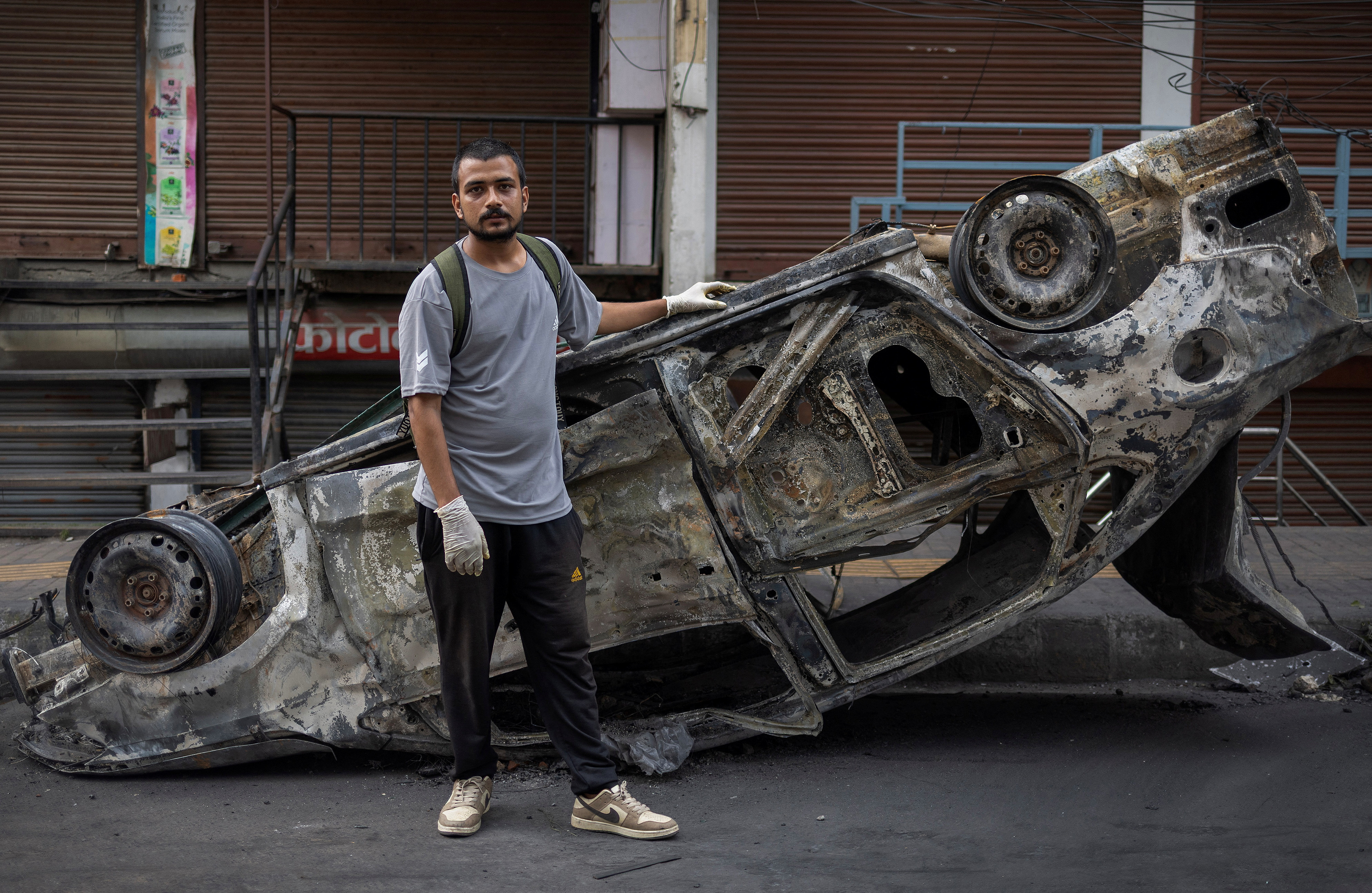 Avash Regmi poses for a photograph while standing next to a burnt car, in Kathmandu