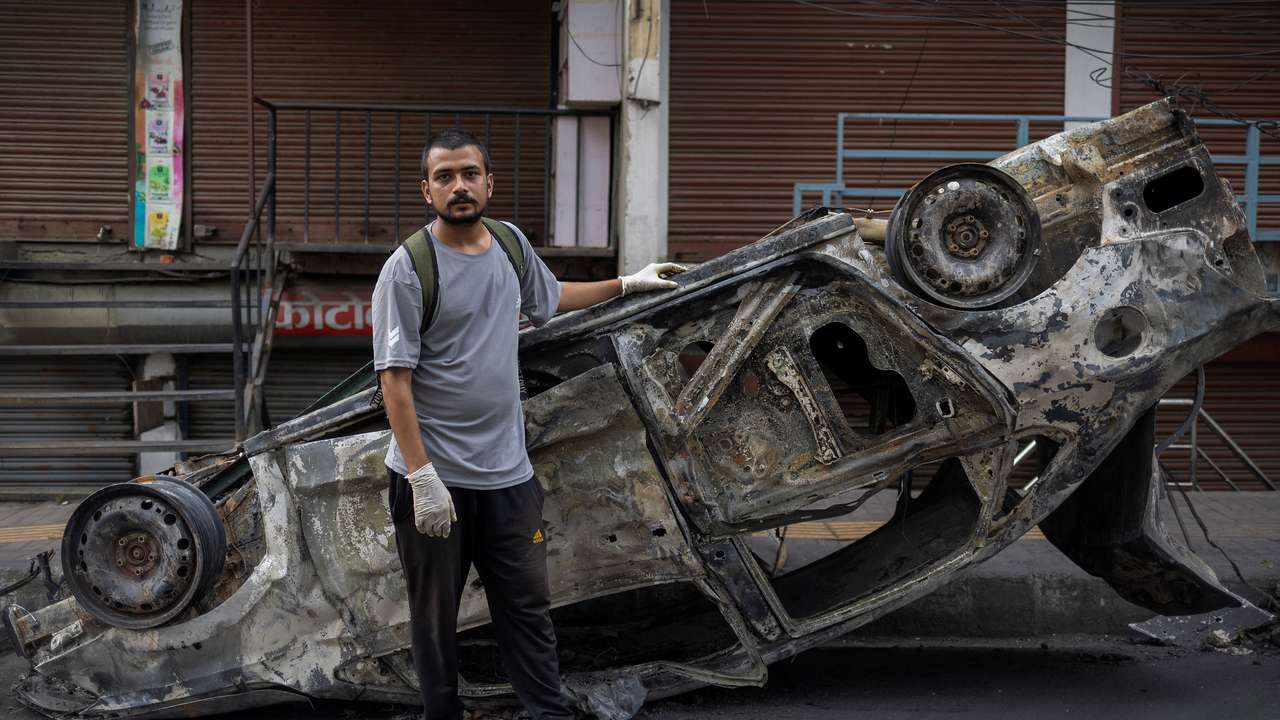 Avash Regmi poses for a photograph while standing next to a burnt car, in Kathmandu