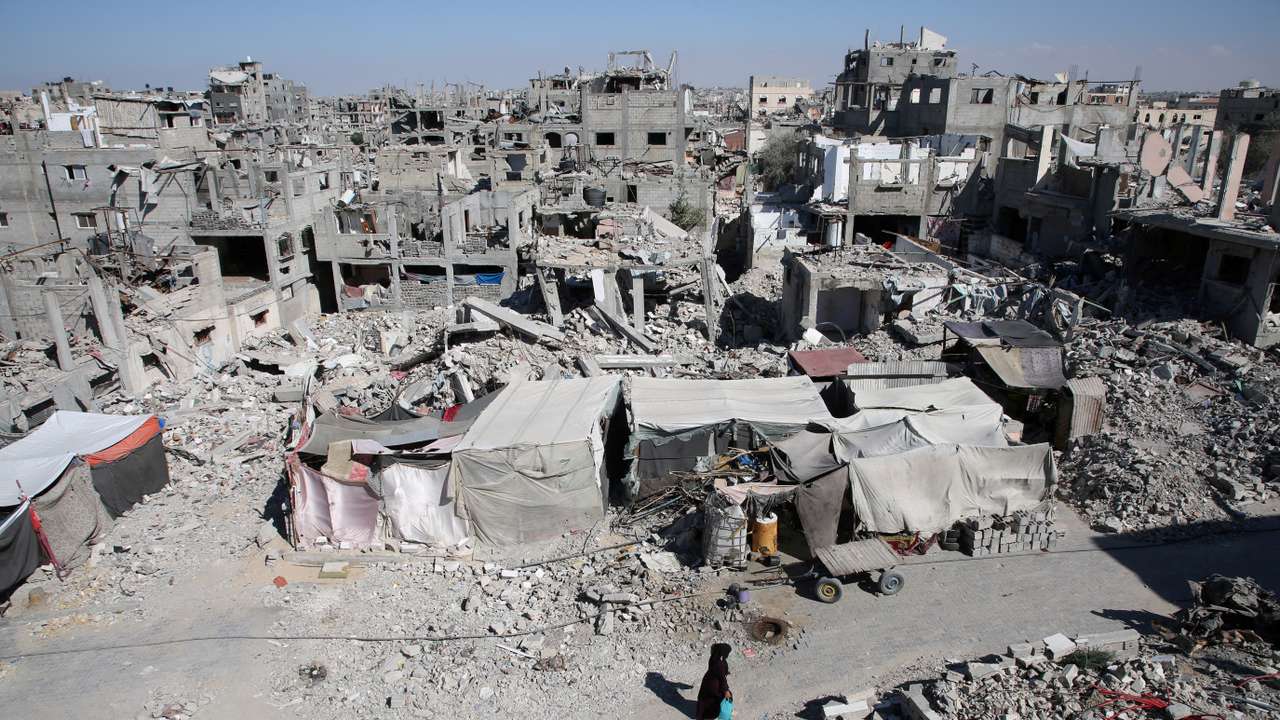 Palestinians walk past the rubble of houses destroyed by Israeli strikes, in Khan Younis