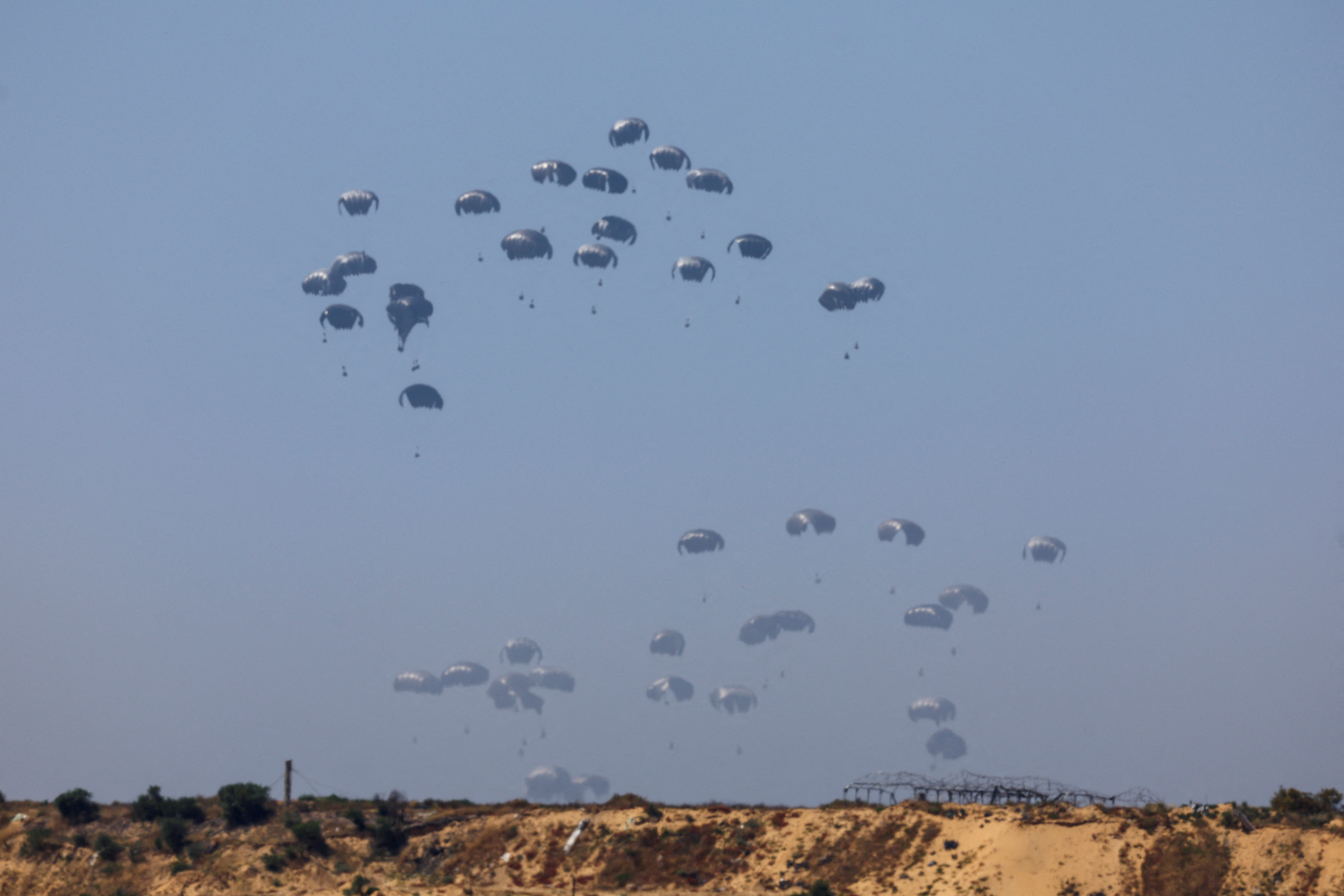 Humanitarian aid falls through the sky towards the Gaza Strip, as seen from Israel