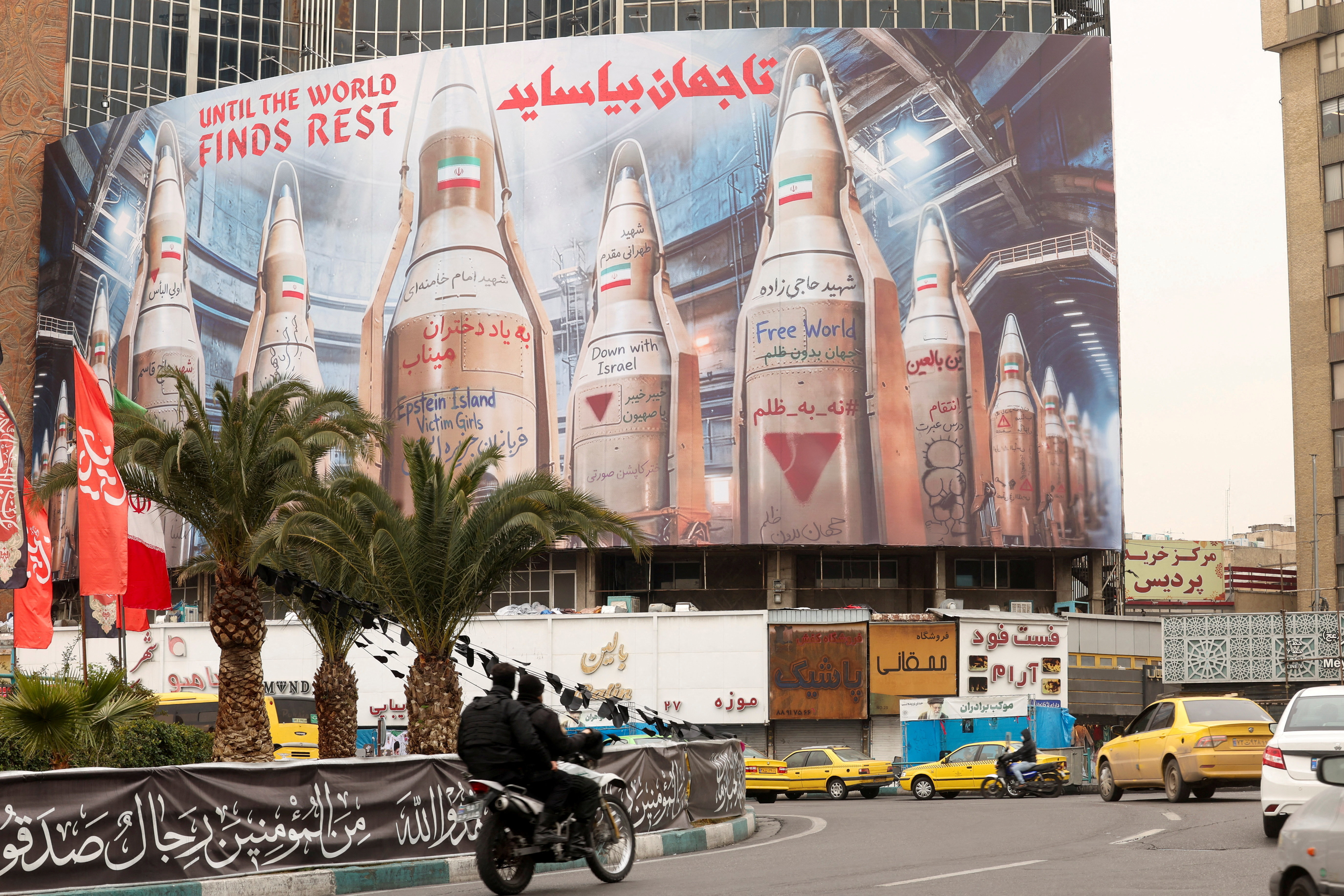 People on motorcycles ride past a large billboard withimages of Iranian missiles, in Tehran