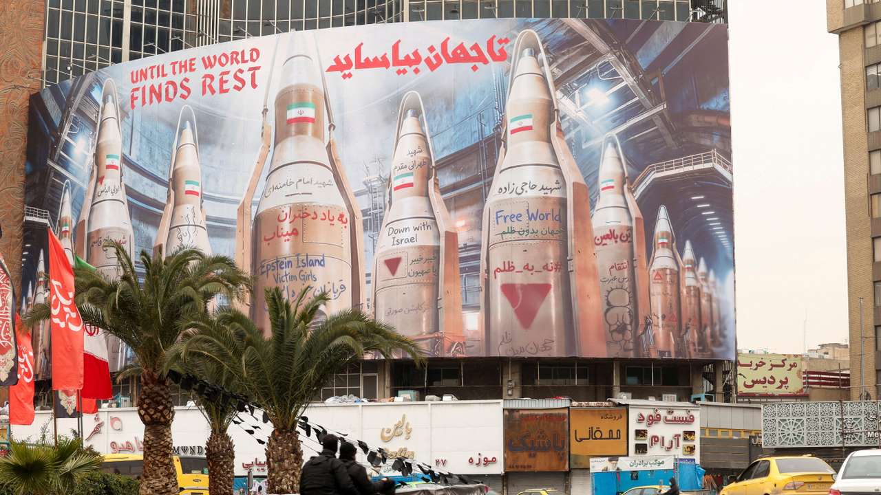 People on motorcycles ride past a large billboard withimages of Iranian missiles, in Tehran