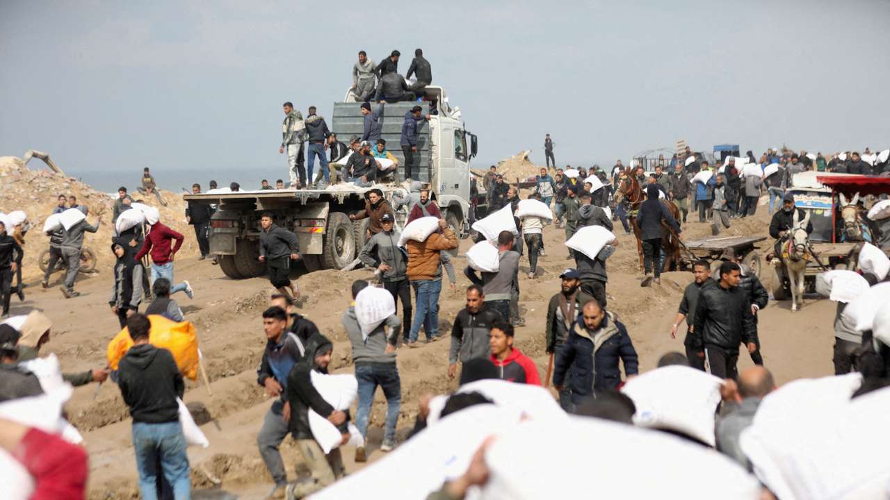 FILE PHOTO: Palestinians carry bags of flour they grabbed from an aid truck near an Israeli checkpoint in Gaza City