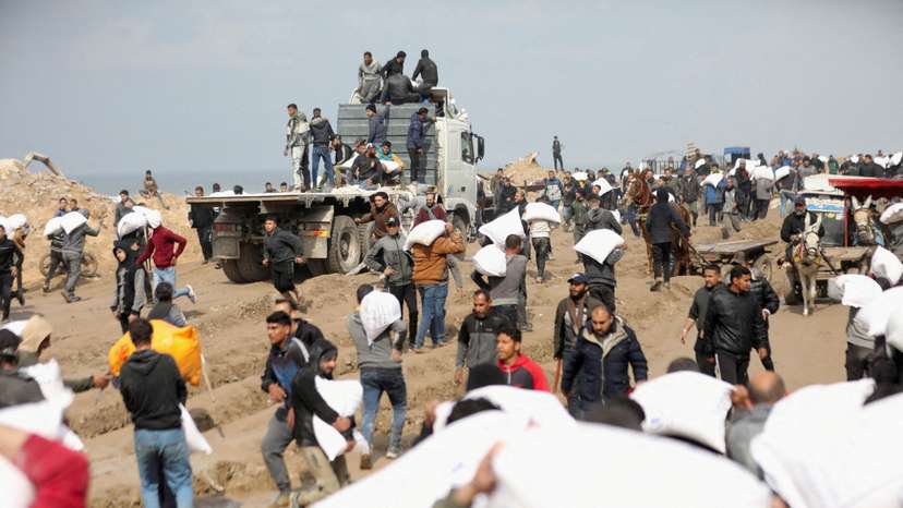 FILE PHOTO: Palestinians carry bags of flour they grabbed from an aid truck near an Israeli checkpoint in Gaza City