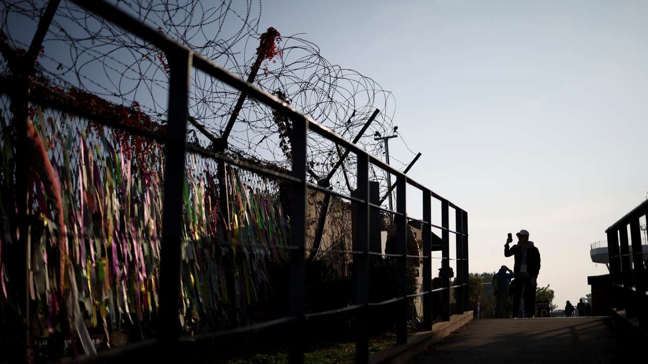 A man takes photographs of his girlfriend in front of a military fence near the demilitarized zone separating the two Koreas
