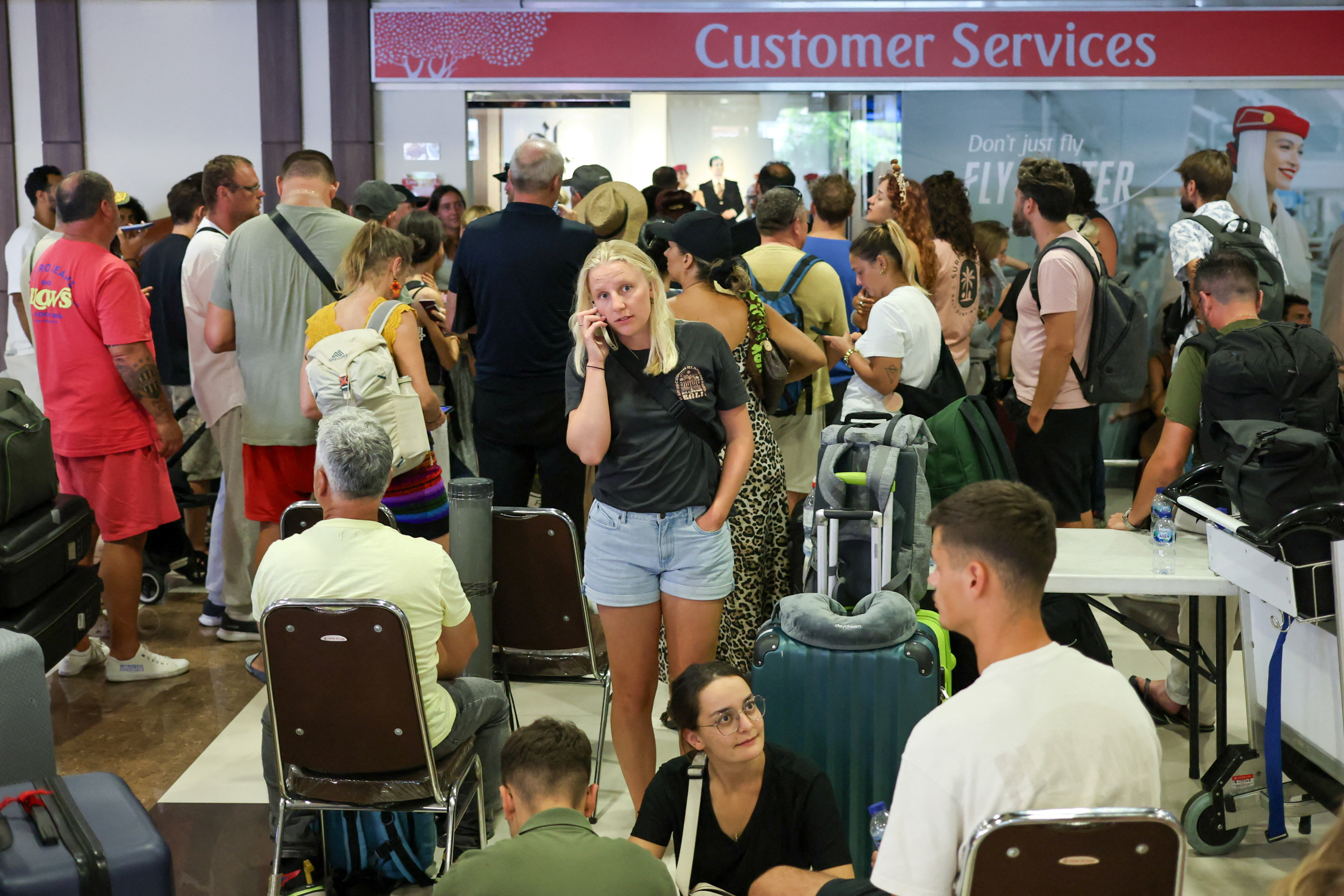 Stranded passengers wait near Emirates Airways customer service office at I Gusti Ngurah Rai International Airport after flights to Doha, Dubai, and Abu Dhabi were cancelled following strikes on Iran launched by the United States and Israel, in Kuta, Bali