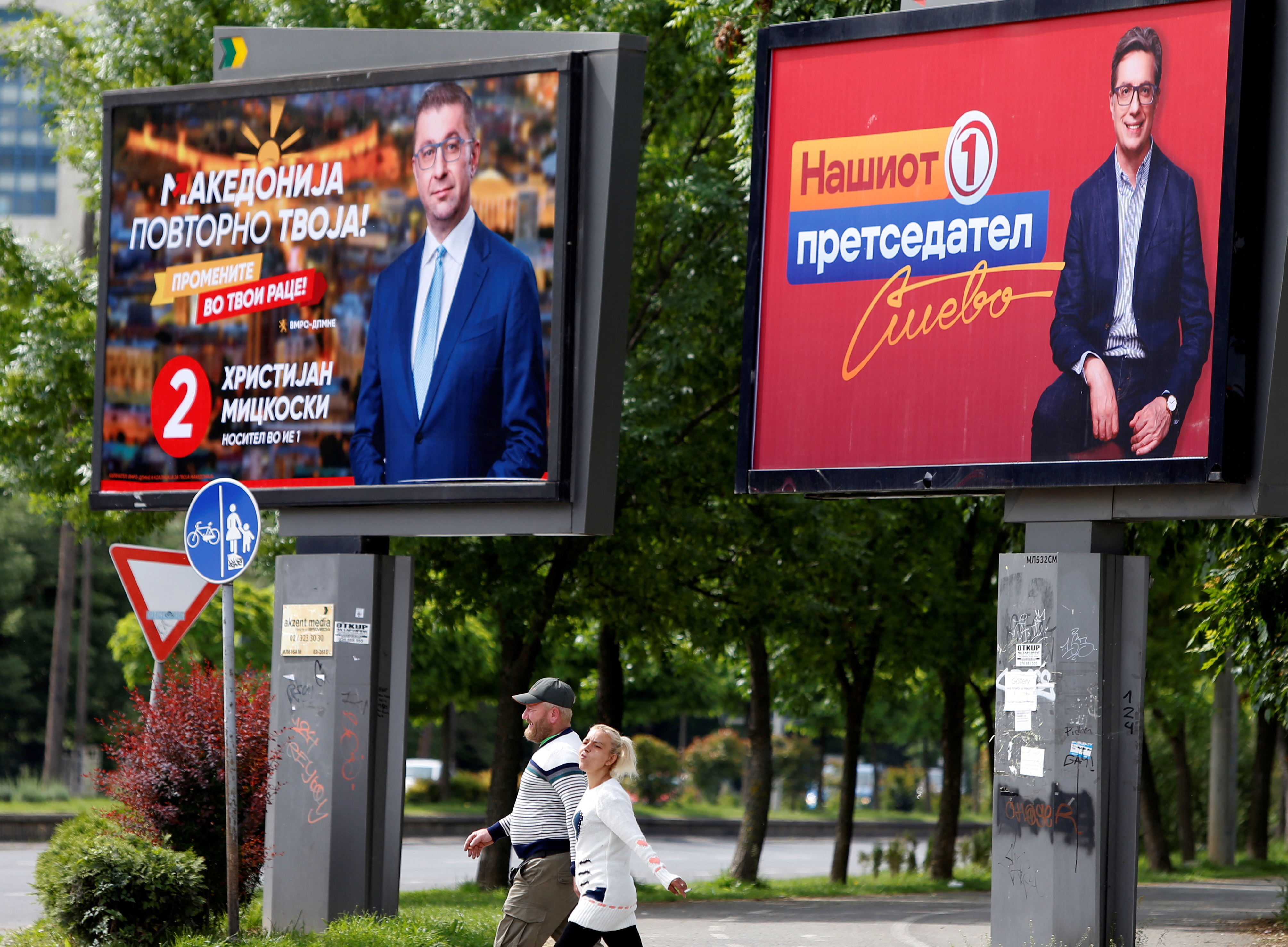 People walk past campaign billboards for the upcoming parliament and presidential elections in Skopje