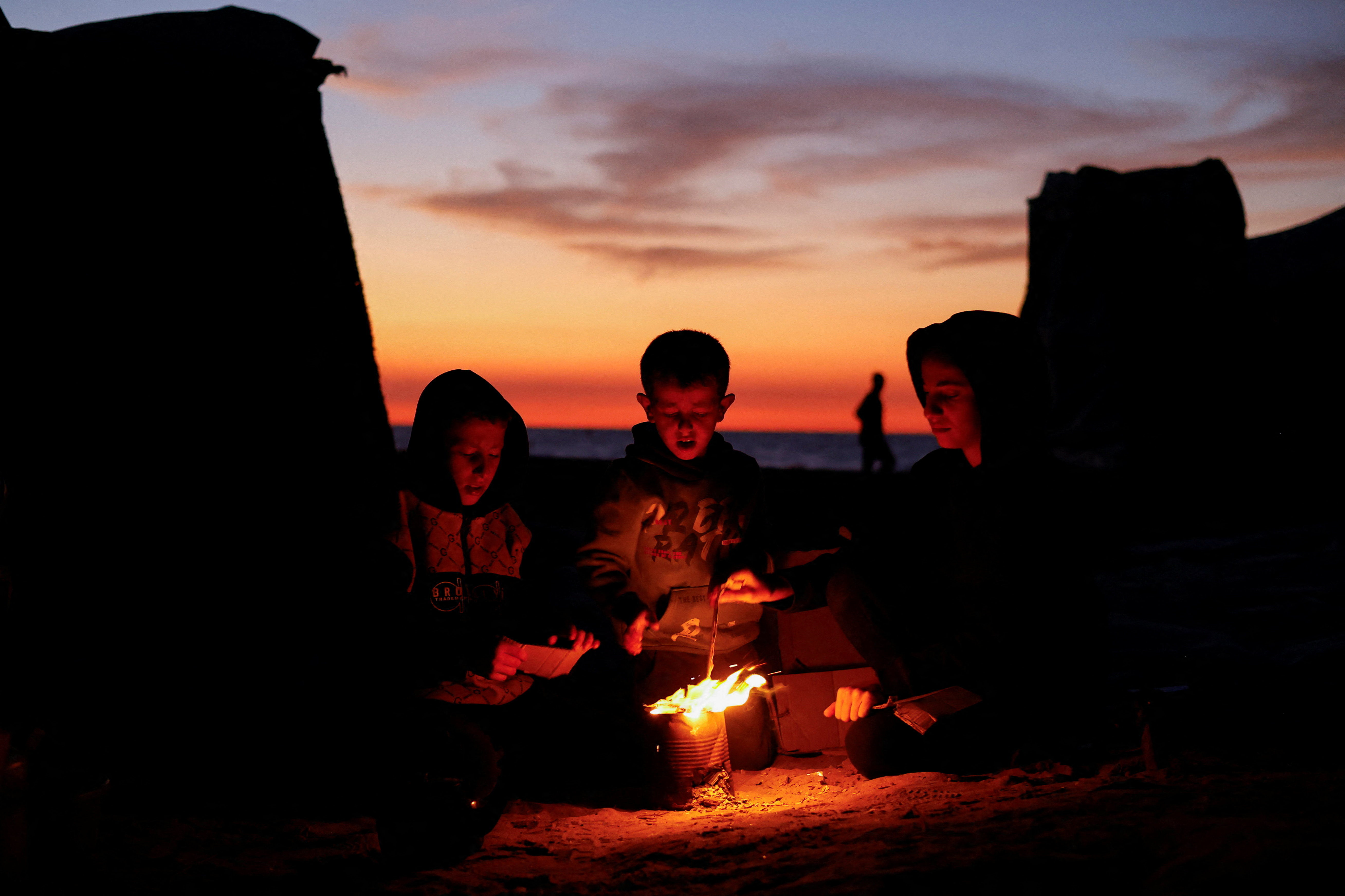 Palestinians sit next to a fire, amid a ceasefire between Israel and Hamas, in Gaza City