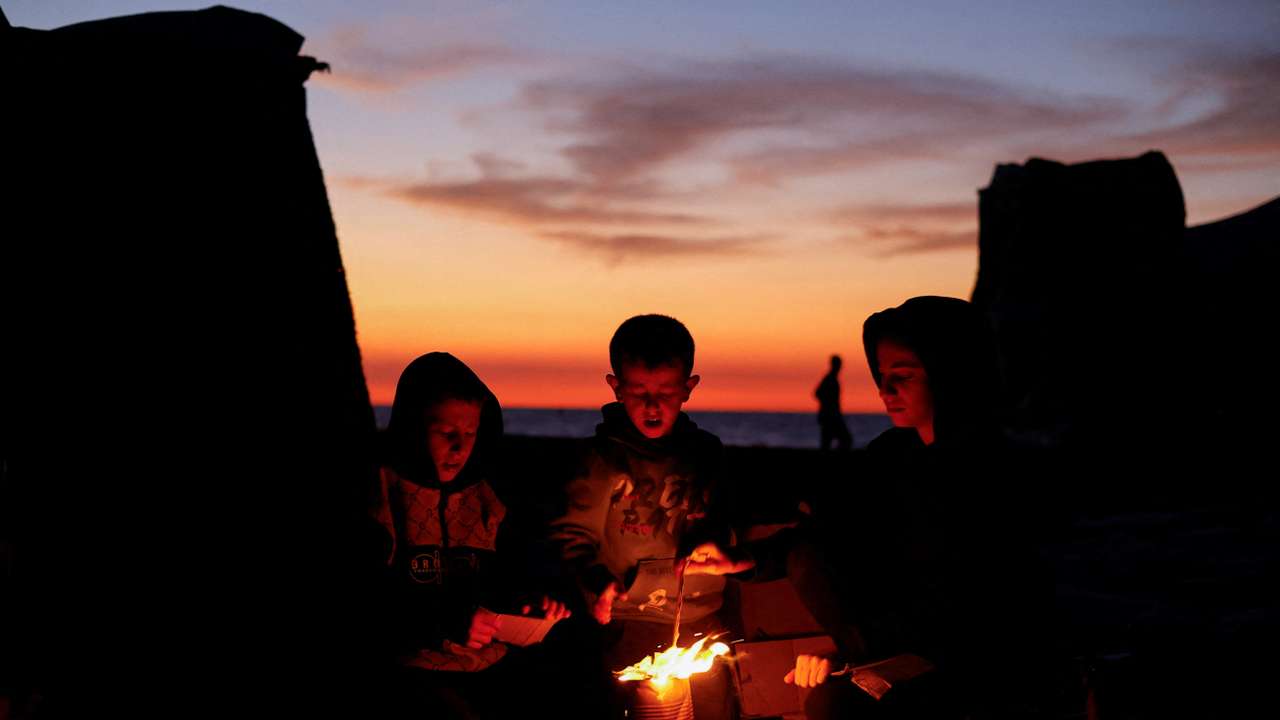 Palestinians sit next to a fire, amid a ceasefire between Israel and Hamas, in Gaza City