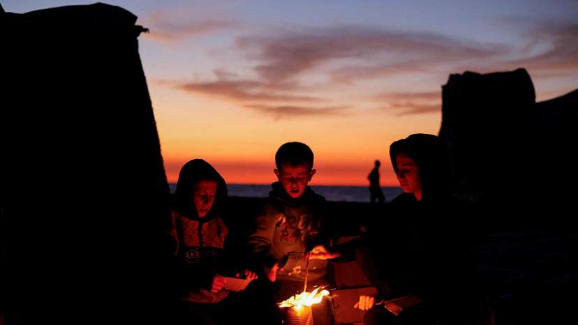 Palestinians sit next to a fire, amid a ceasefire between Israel and Hamas, in Gaza City