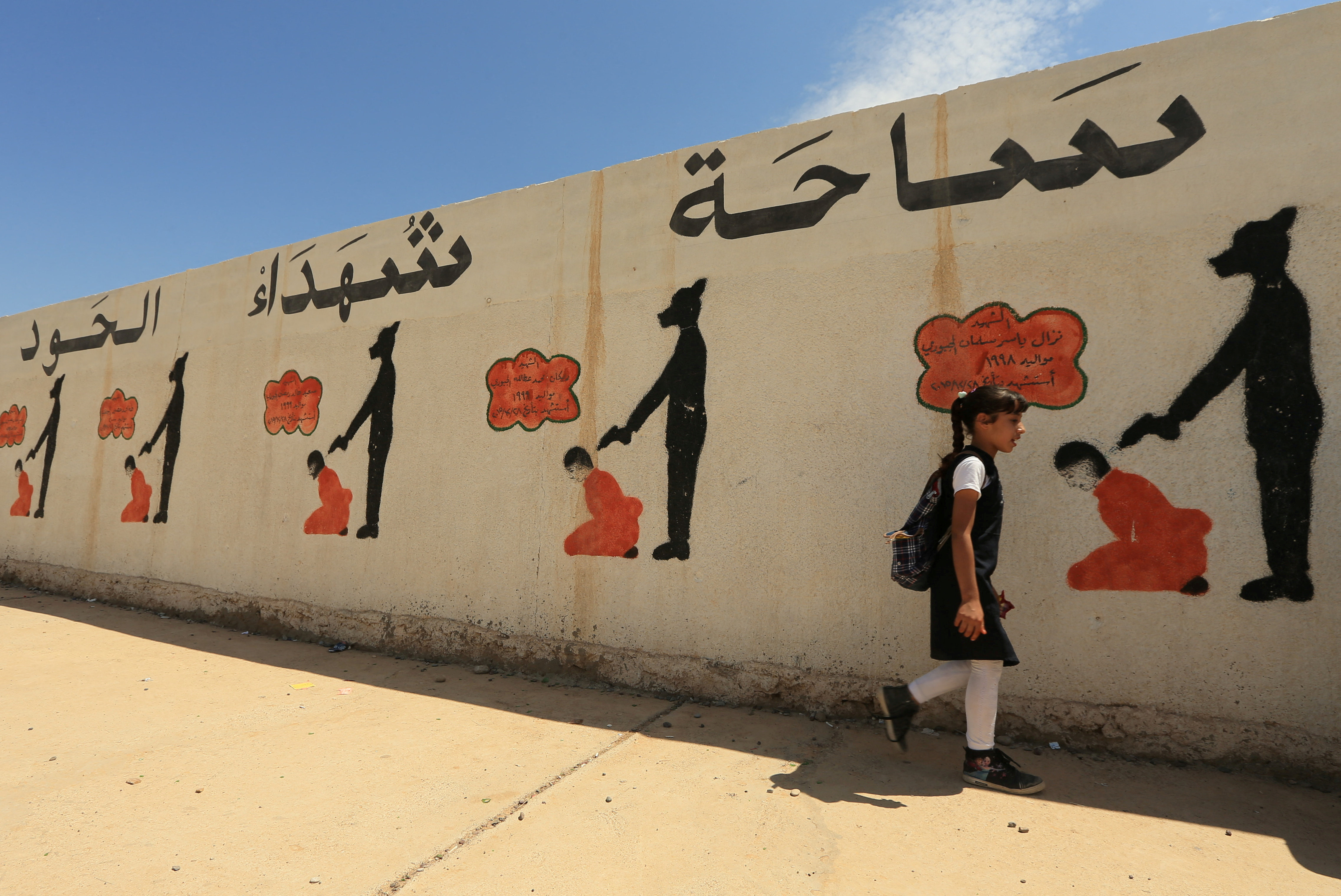 FILE PHOTO: An Iraqi student walks past a school wall covered with drawings showing how Islamic State militants executed their prisoners in Mosul