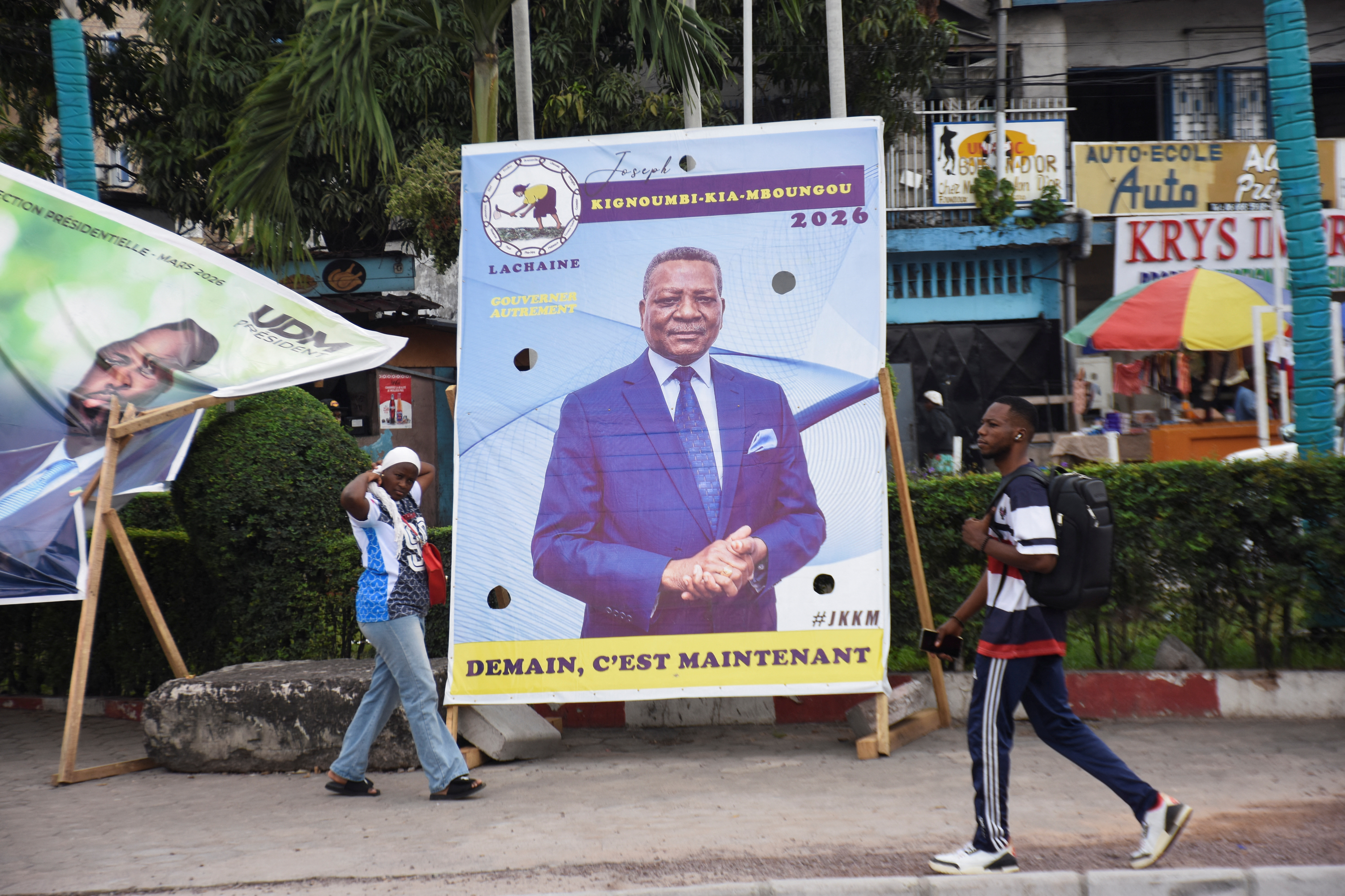 People walk past a campaign billboard of the presidential candidate, Joseph Kignoumbi Kia Mboungou, leader of La Chaine party, in Brazzaville