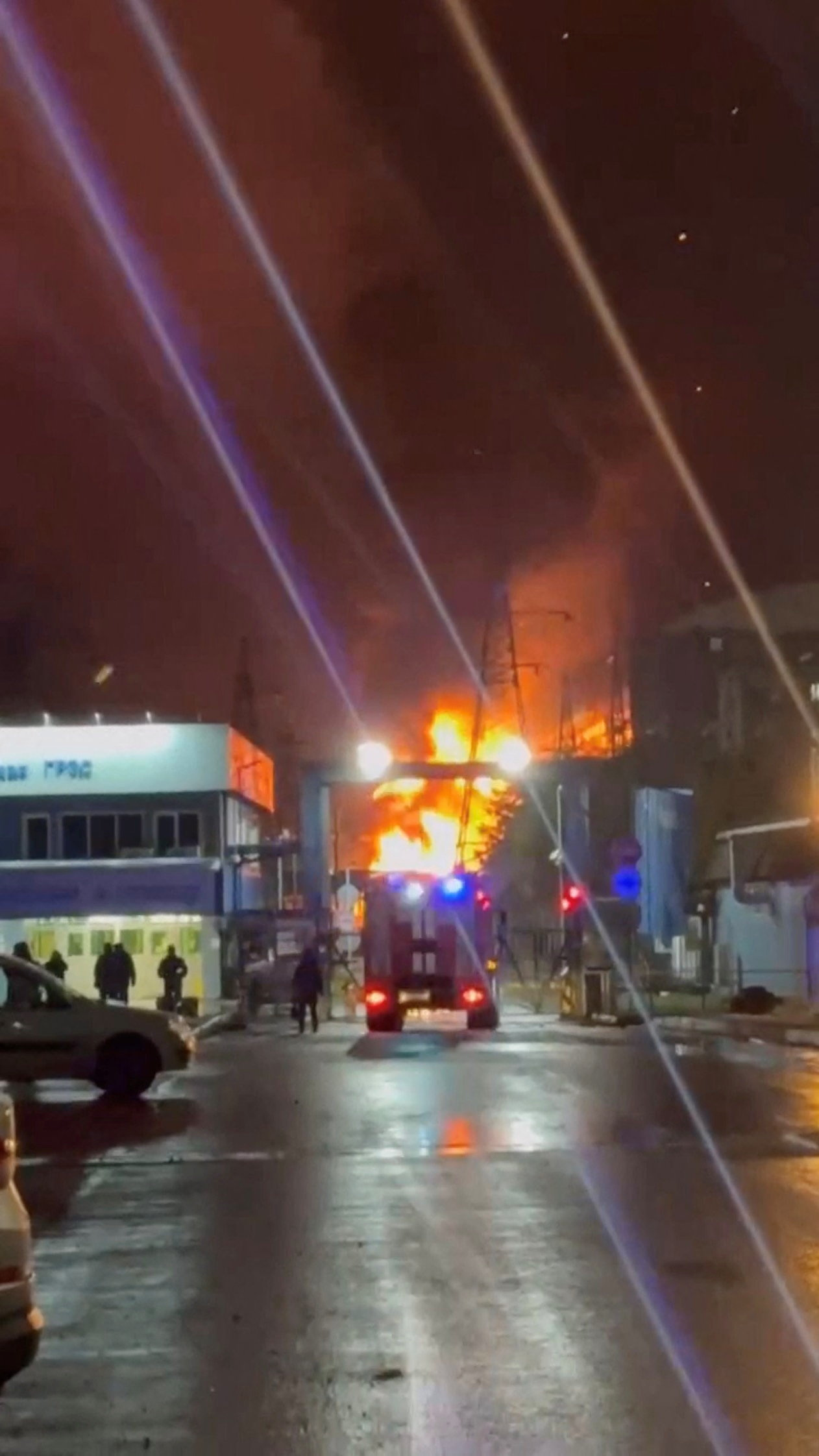 A person stands by an emergency vehicle as fire and smoke rise around the Shatura Power Station in Shatura