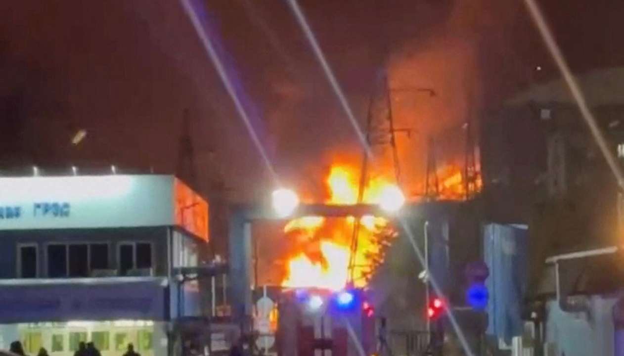 A person stands by an emergency vehicle as fire and smoke rise around the Shatura Power Station in Shatura