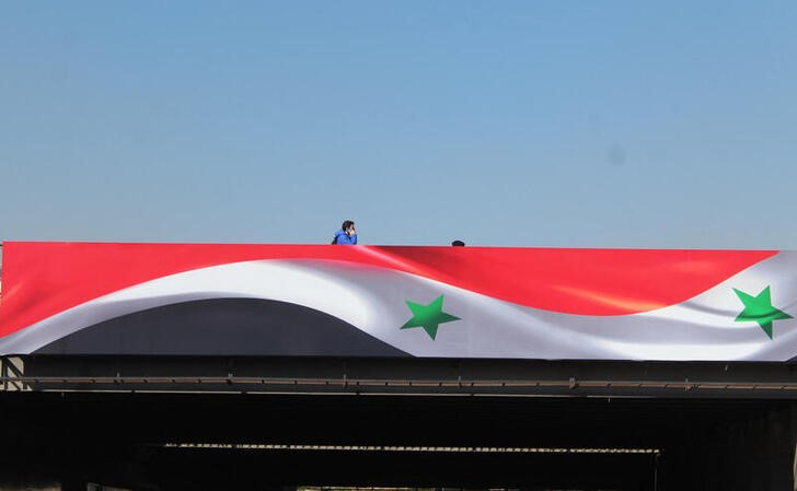 A man walks near a sign depicting the Syrian flag in Damascus