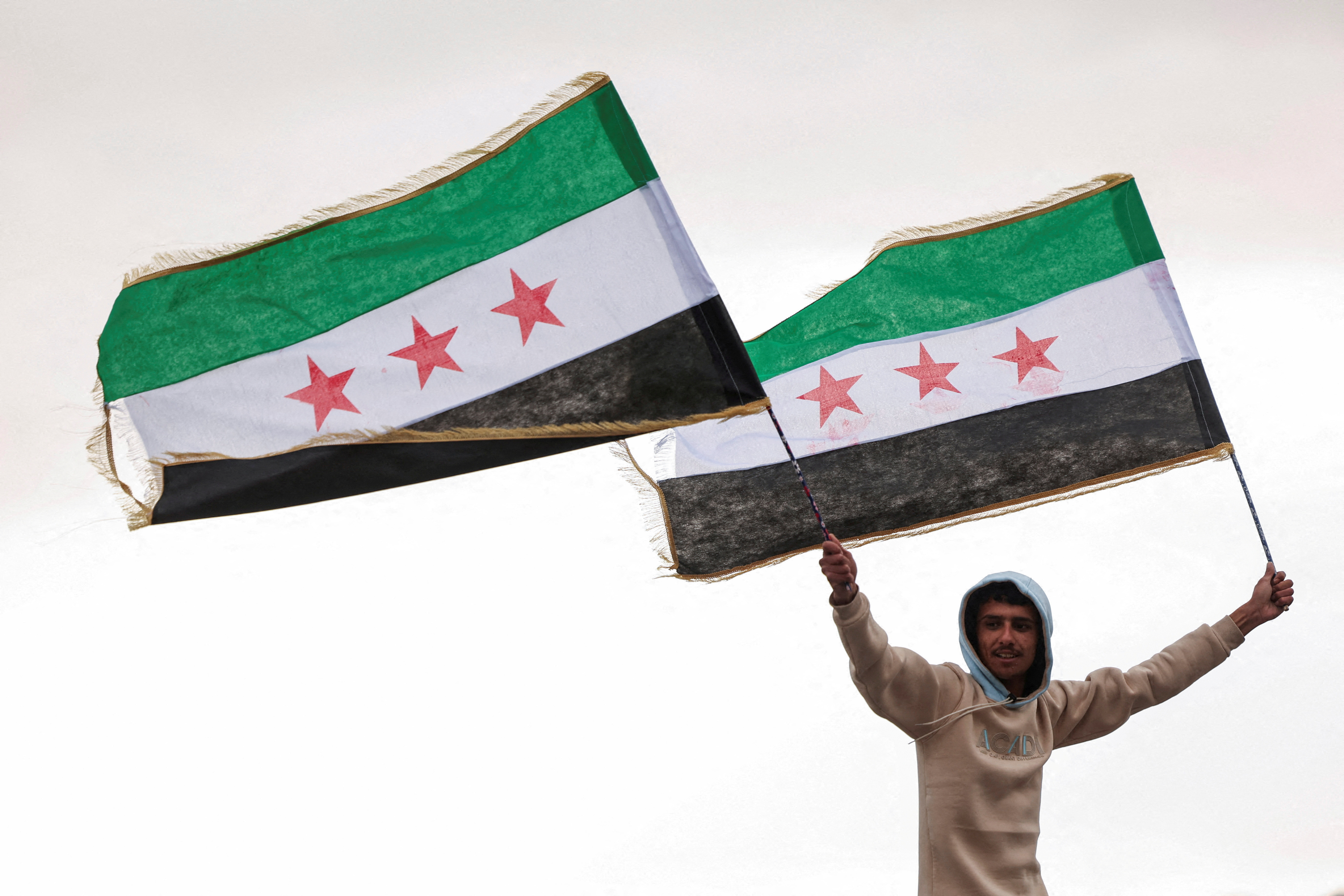 FILE PHOTO: A person holds flags adopted by the new Syrian rulers, in Damascus
