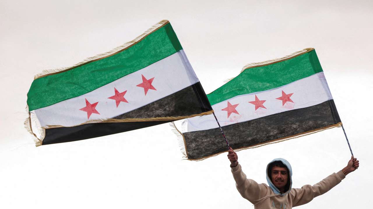 FILE PHOTO: A person holds flags adopted by the new Syrian rulers, in Damascus