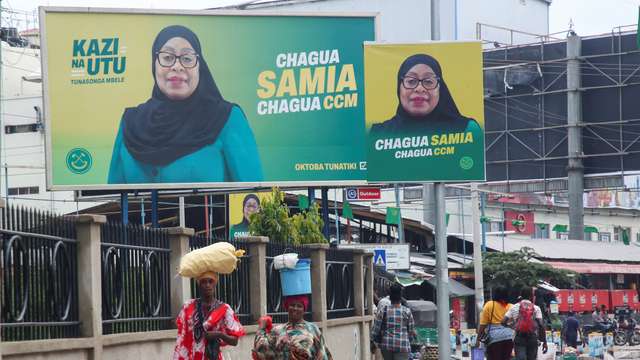 People walk past electoral campaign billboards of Tanzania's President Samia Suluhu Hassan of the ruling CCM ahead of the general elections in Ilala district of Dar es Salaam