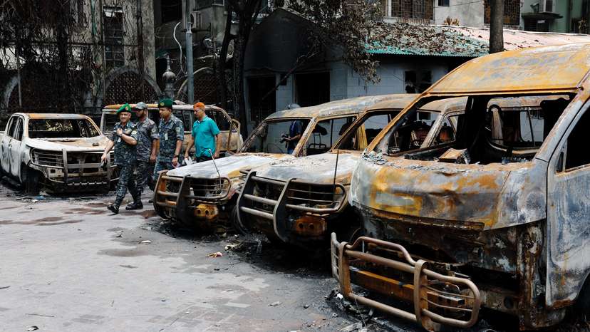 Security personnel walk past damaged vehicles of a government owned organization, that were set afire by a mob during clashes after violence erupted following protests by students against government job quotas, in Dhaka