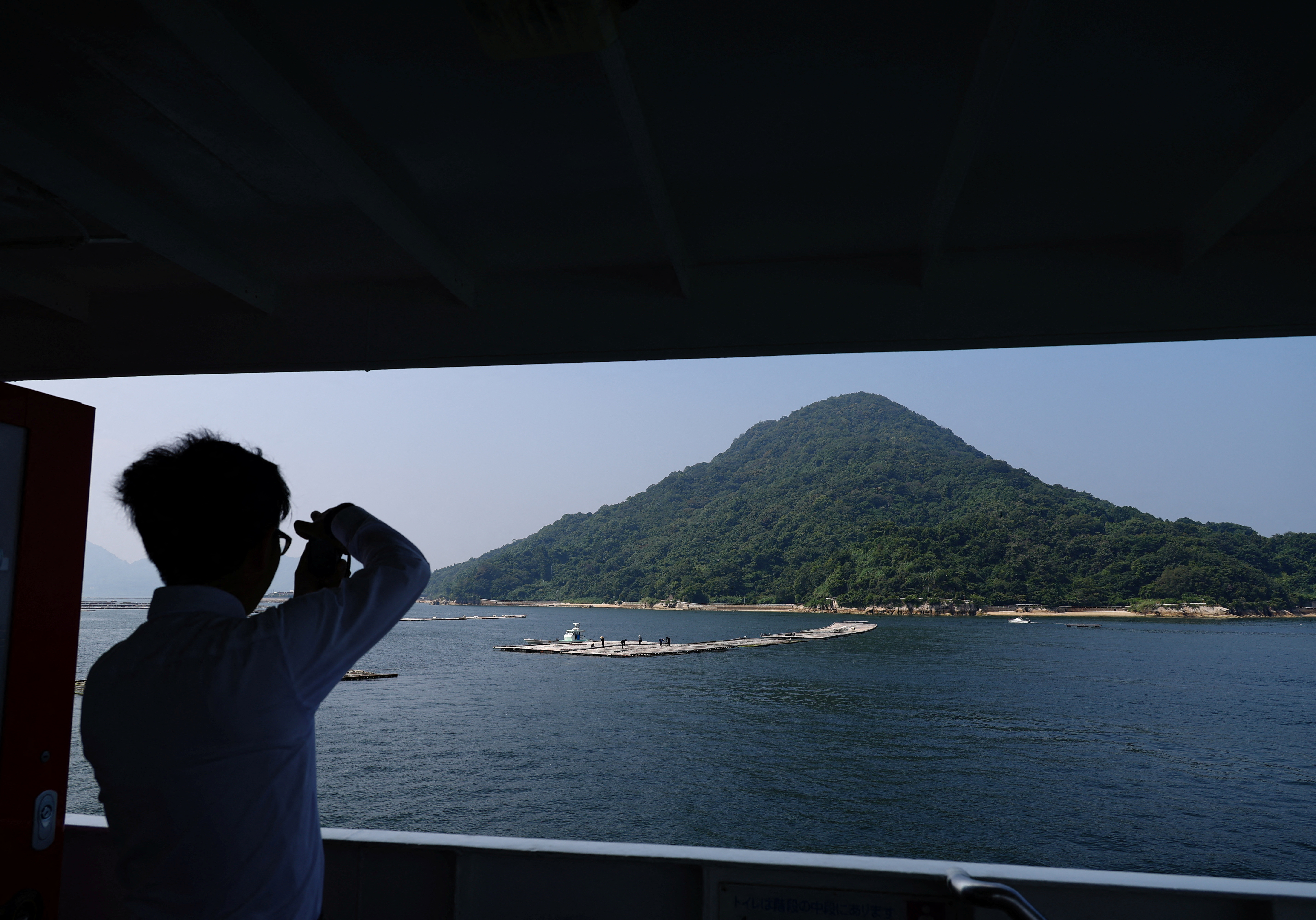 Rebun Kayo takes a photo of Ninoshima Island from a ferry approaching the island, where remains of atomic bomb victims are believed to remain buried since 1945