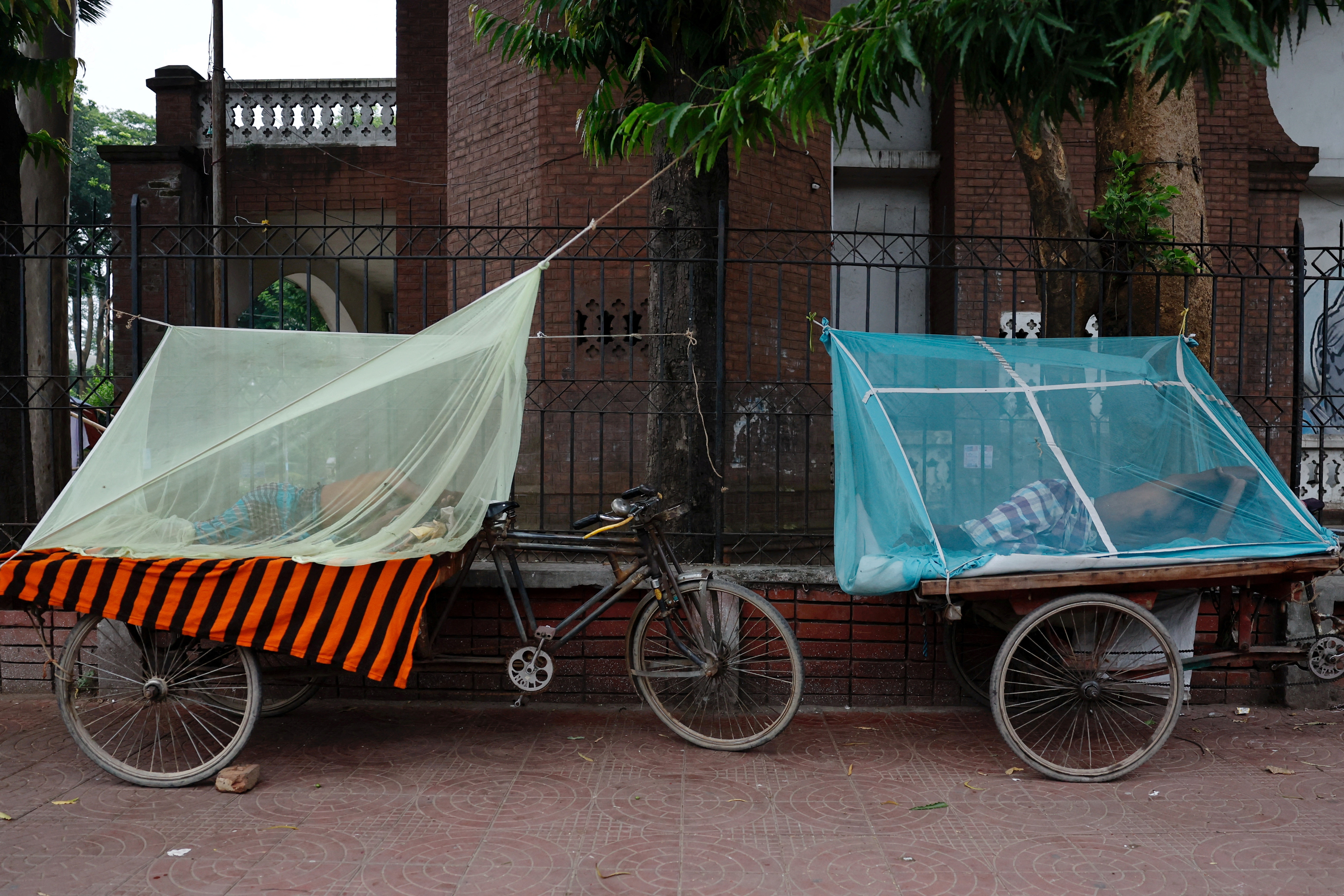 FILE PHOTO: People sleep on three-wheeler carts using mosquito nets, following a surge of dengue-infected patients in Dhaka