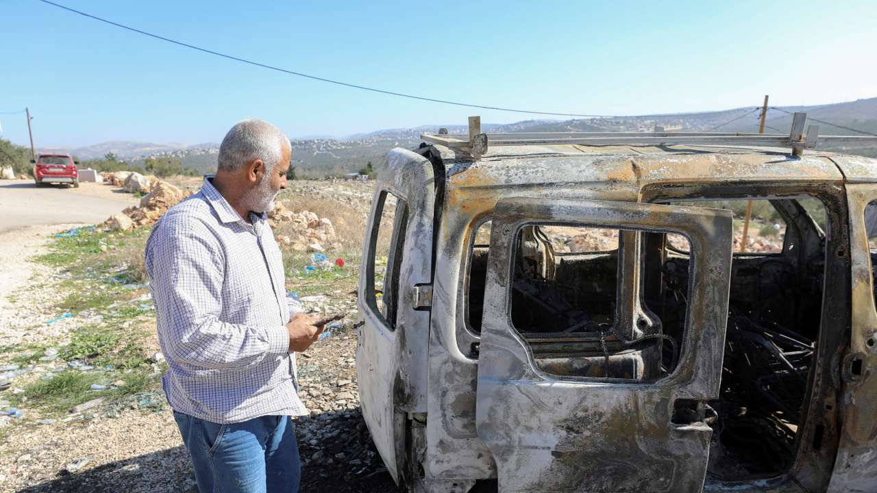 A Palestinian checks a car burned in Israeli settlers raid near Salfit in the West Bank