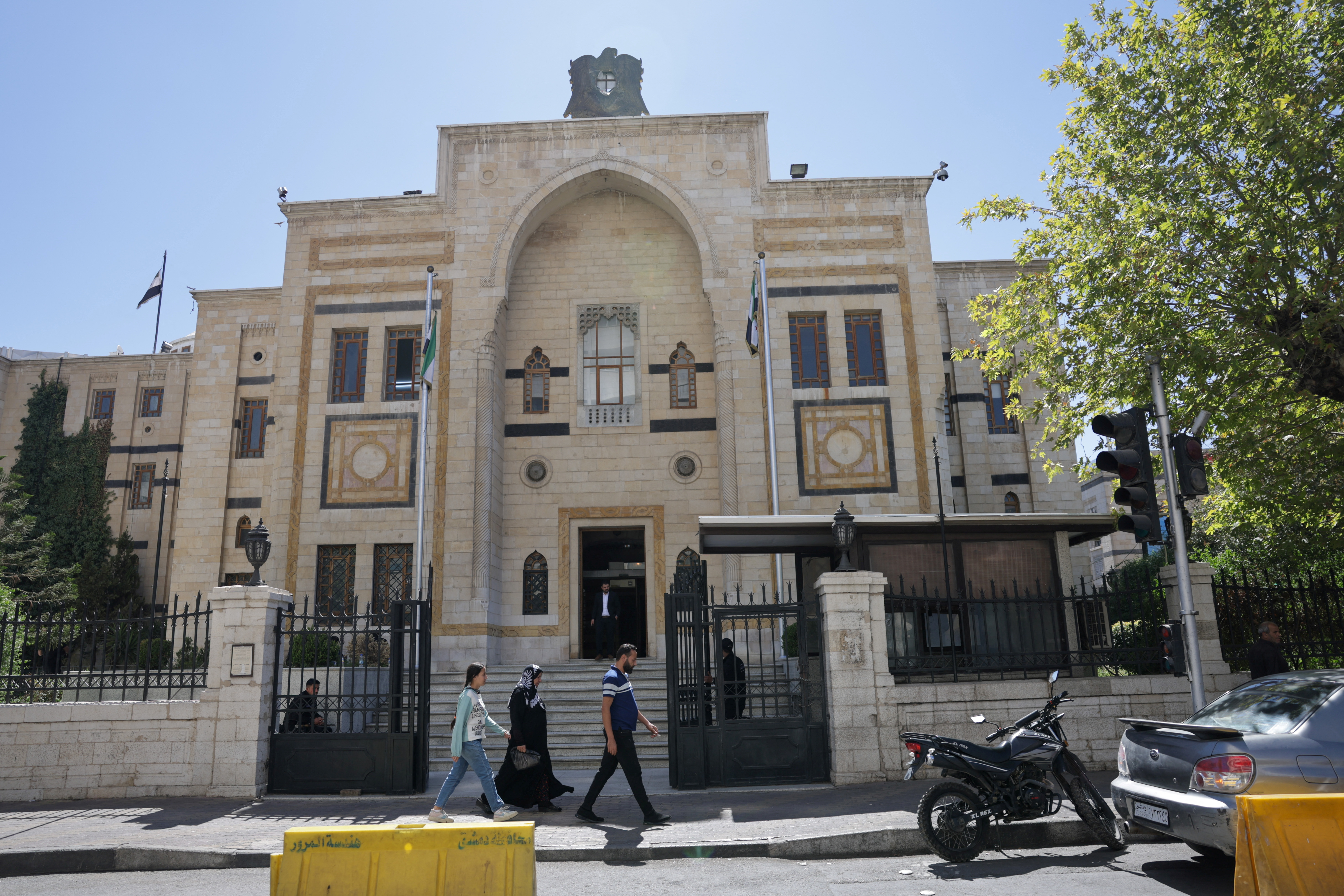 A group of civilians walk past the main gate of the Syrian parliament building, in Damascus