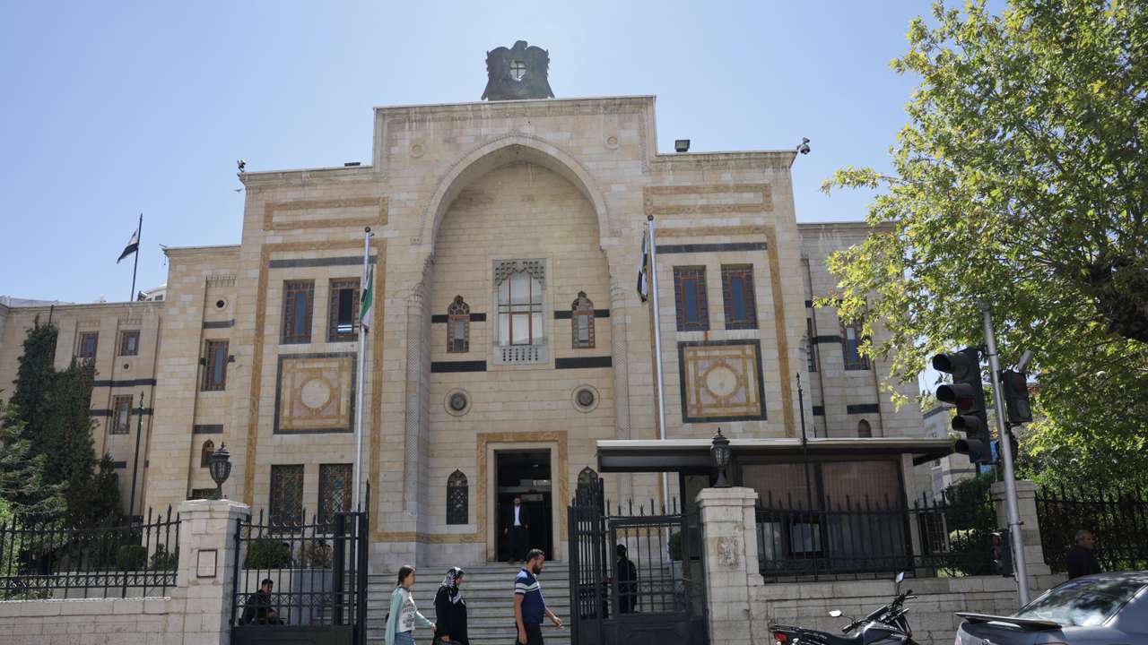 A group of civilians walk past the main gate of the Syrian parliament building, in Damascus