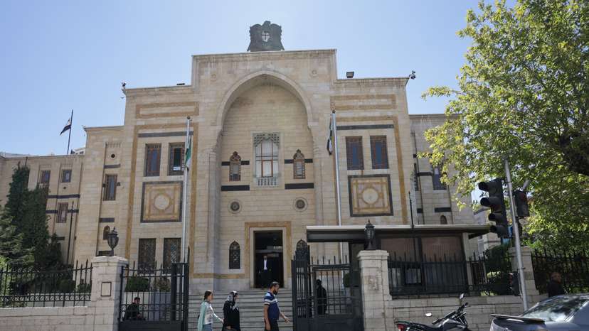 A group of civilians walk past the main gate of the Syrian parliament building, in Damascus